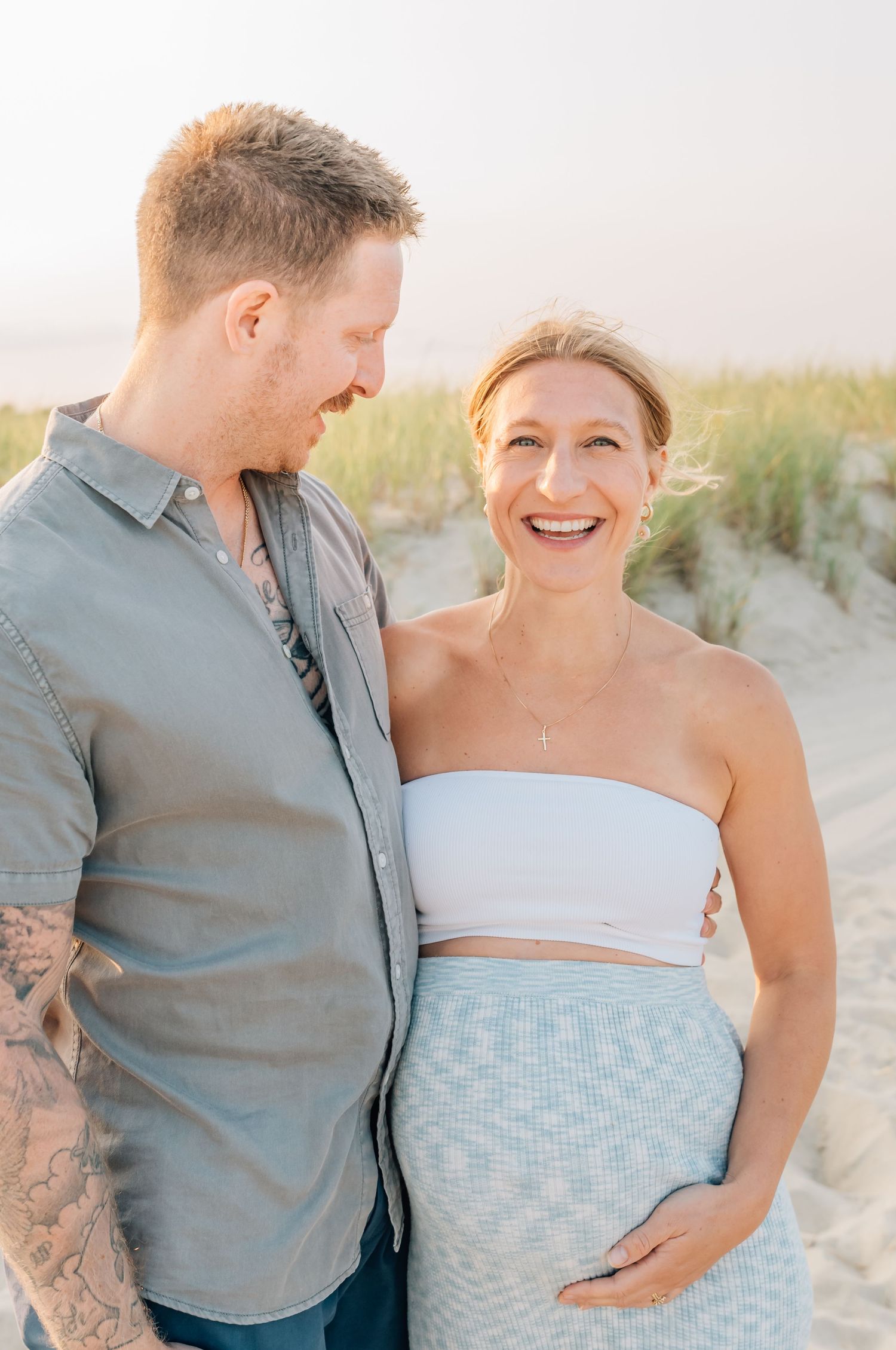 A pregnant woman and her partner laugh together on the spring lake beach.