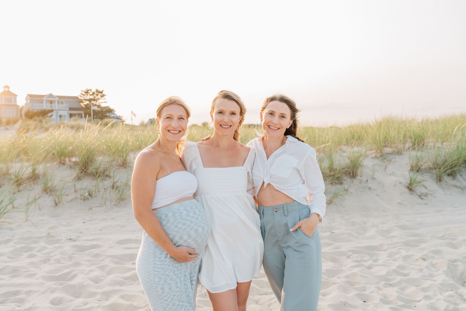 A portrait of sisters in white and green smiling on the beach in front of dunes in Monmouth County Nj.
