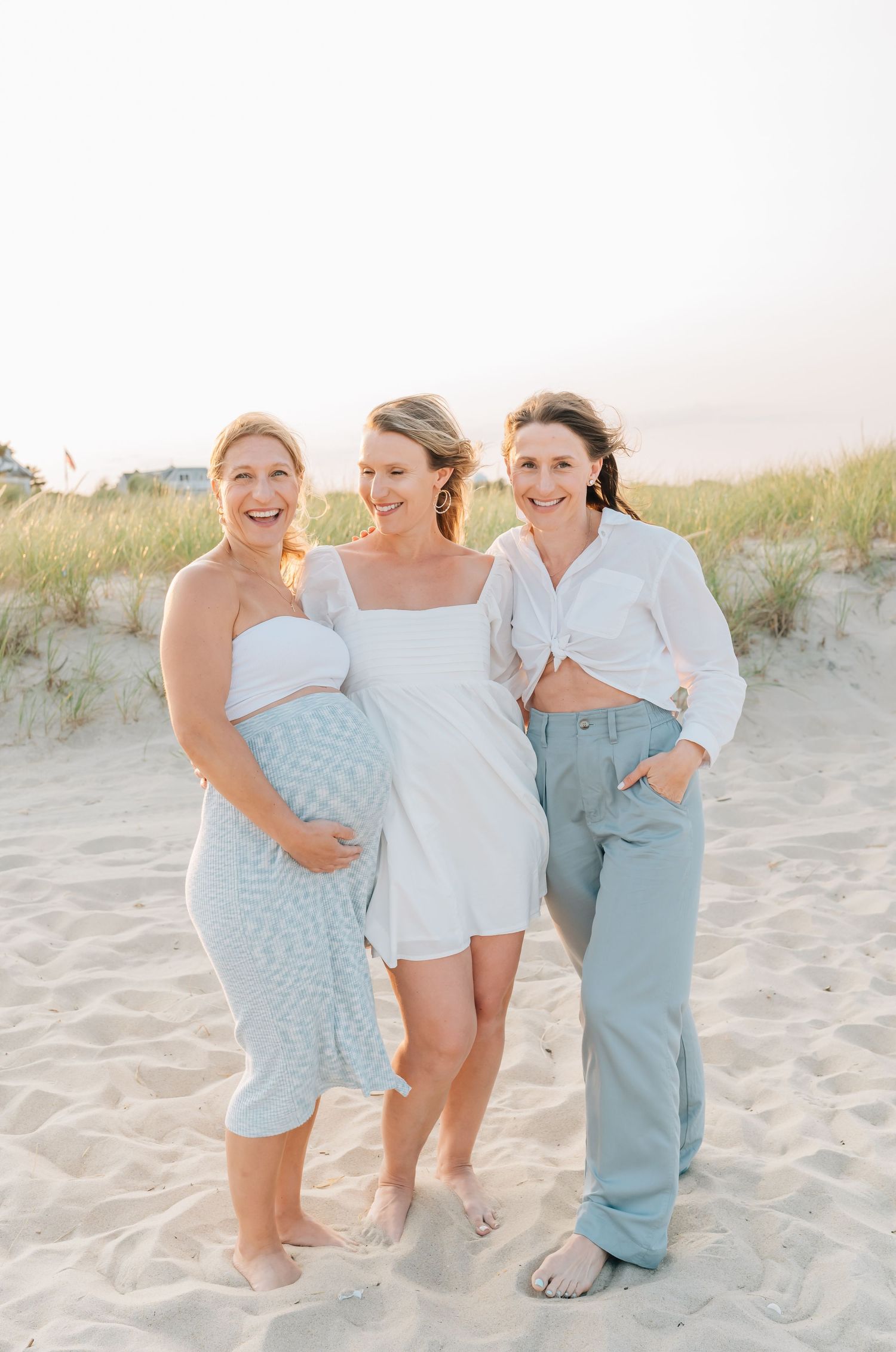 Three adult sisters stand together on the beach in spring lake during an extended family session.