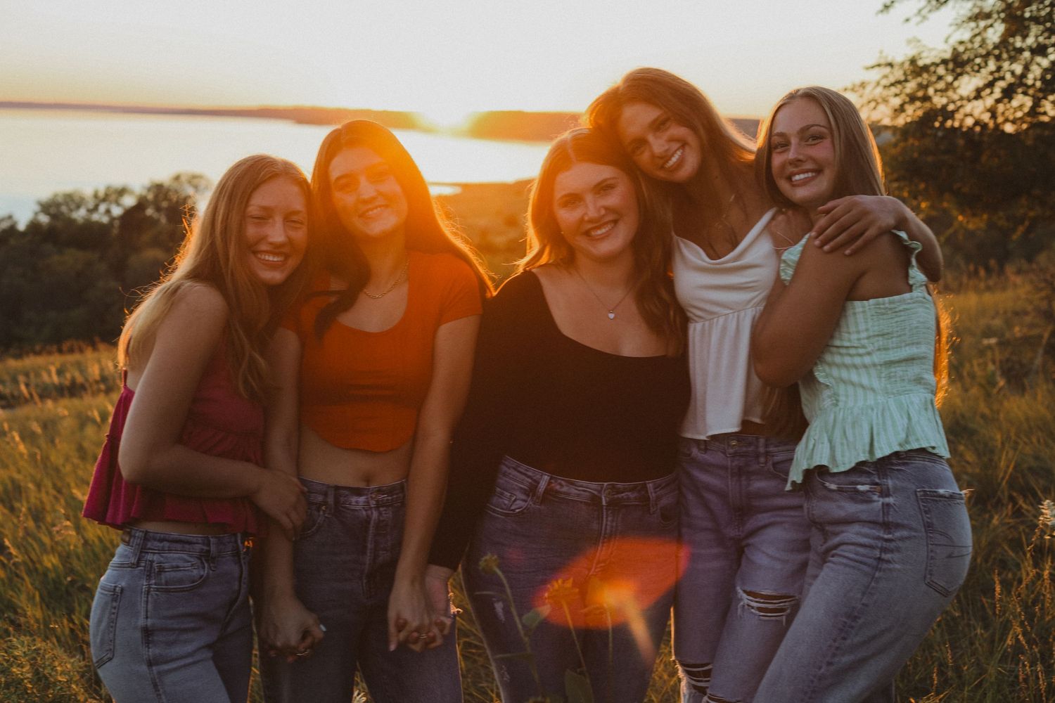 Group of friends laughing together during golden hour sunset in a field.