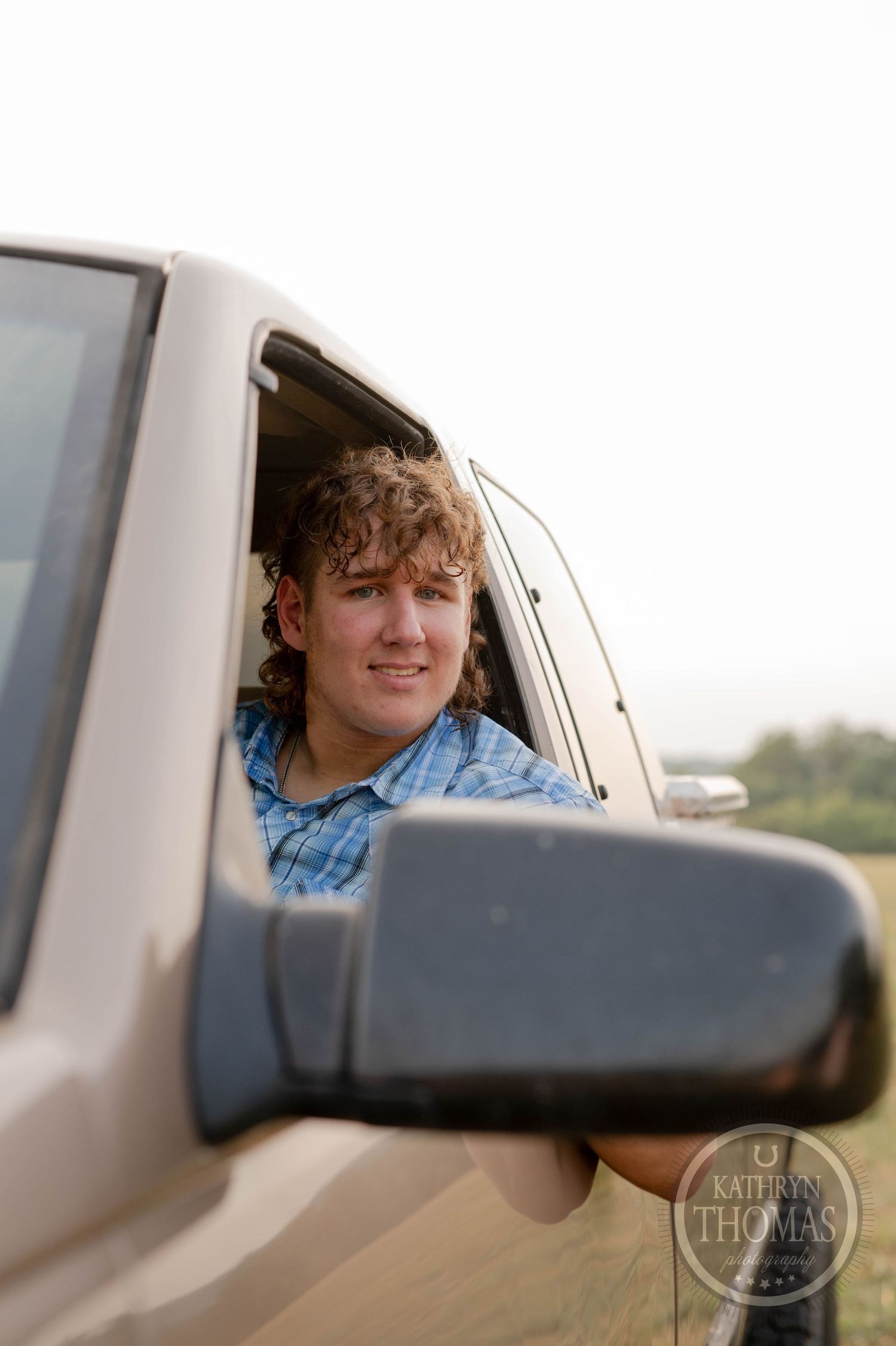 Someone smiling through the driver's window of a tan pickup truck.
