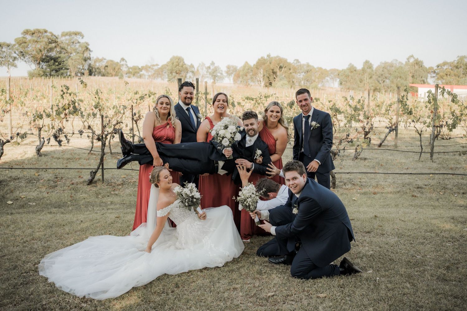 A wedding party poses together on a dirt road surrounded by tall eucalyptus trees.