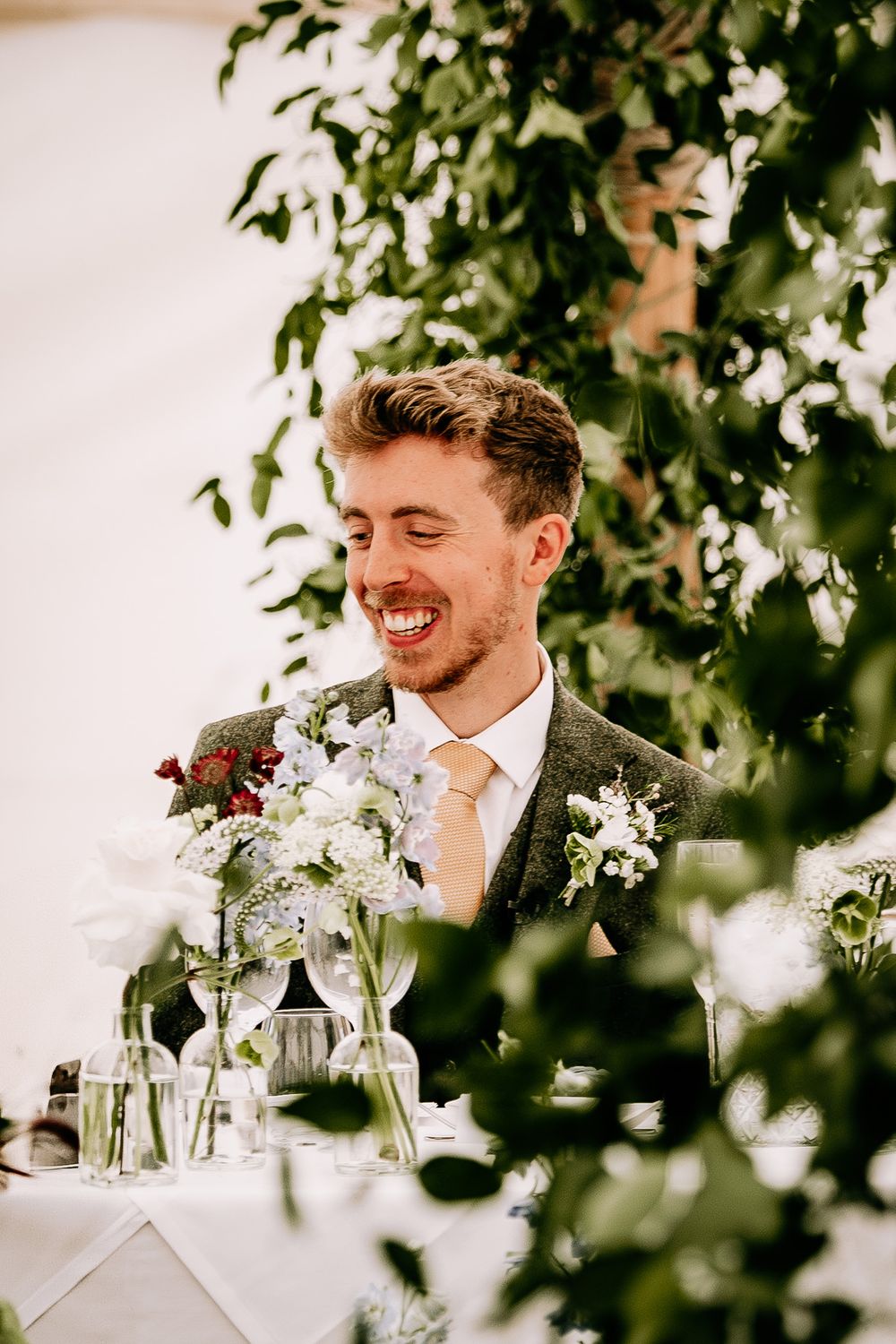 Wedding reception table decorated with delicate white flowers in glass vases under hanging greenery.