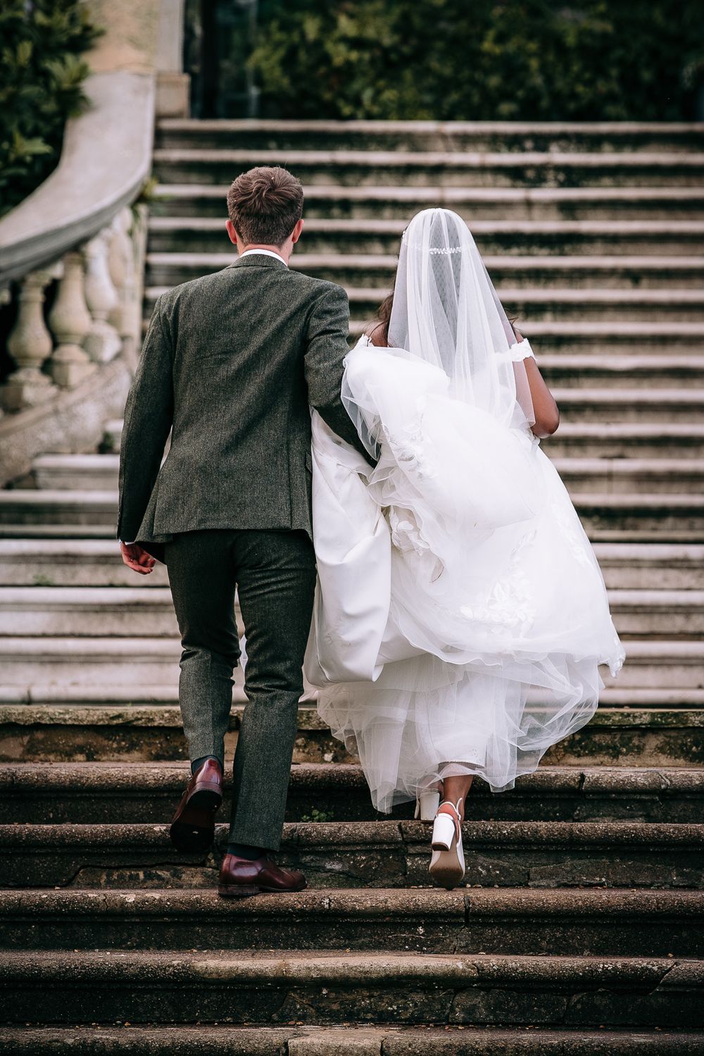 Couple ascending stone steps together, with focus on wedding dress and formal attire details.