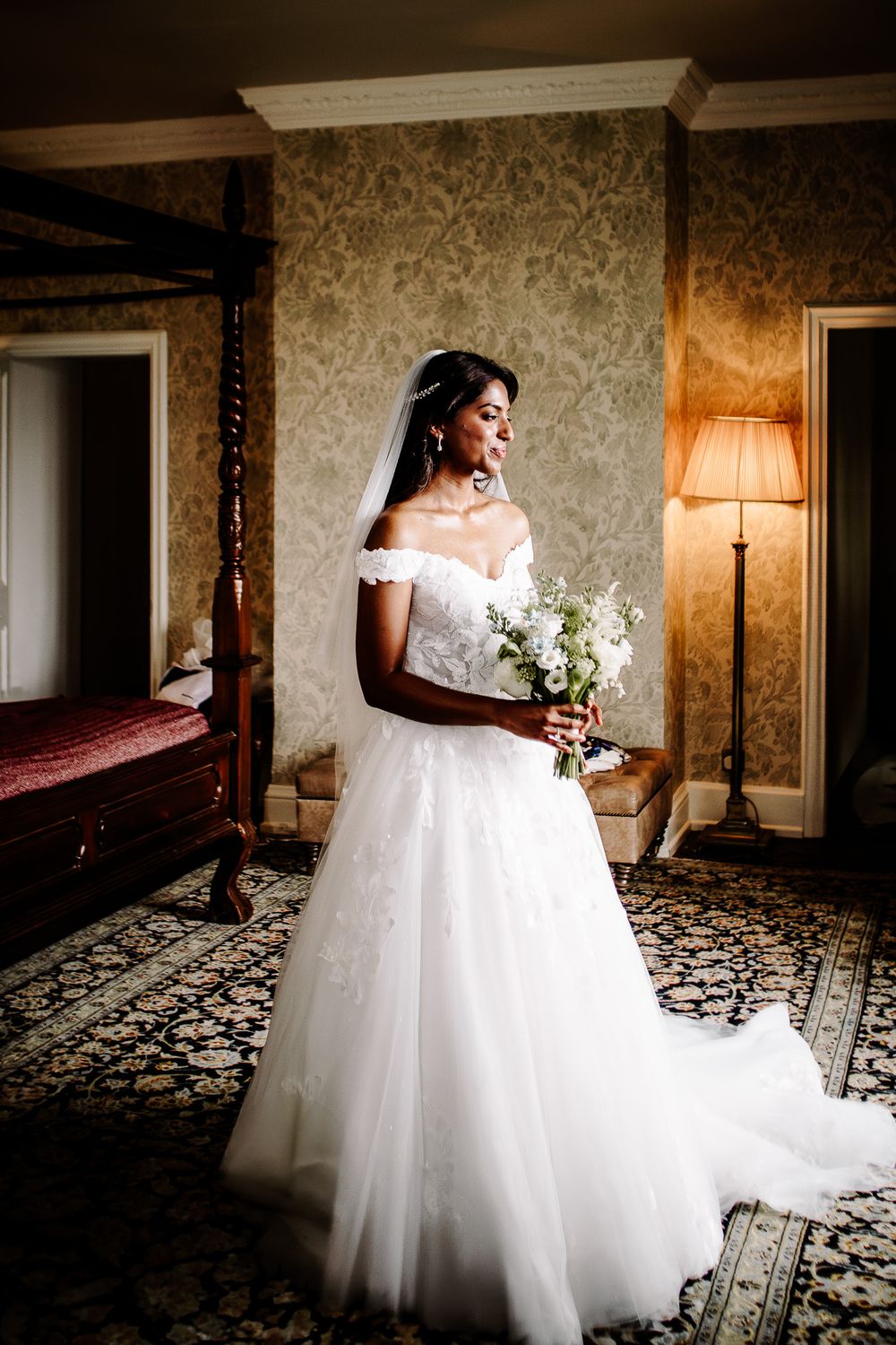 Elegant bridal portrait in a luxurious room with ornate wallpaper and flowing white gown.