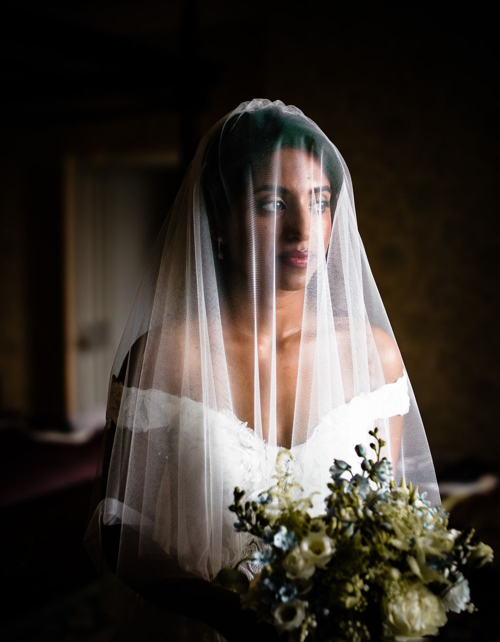 Artistic bridal portrait through sheer white veil with soft floral accents.