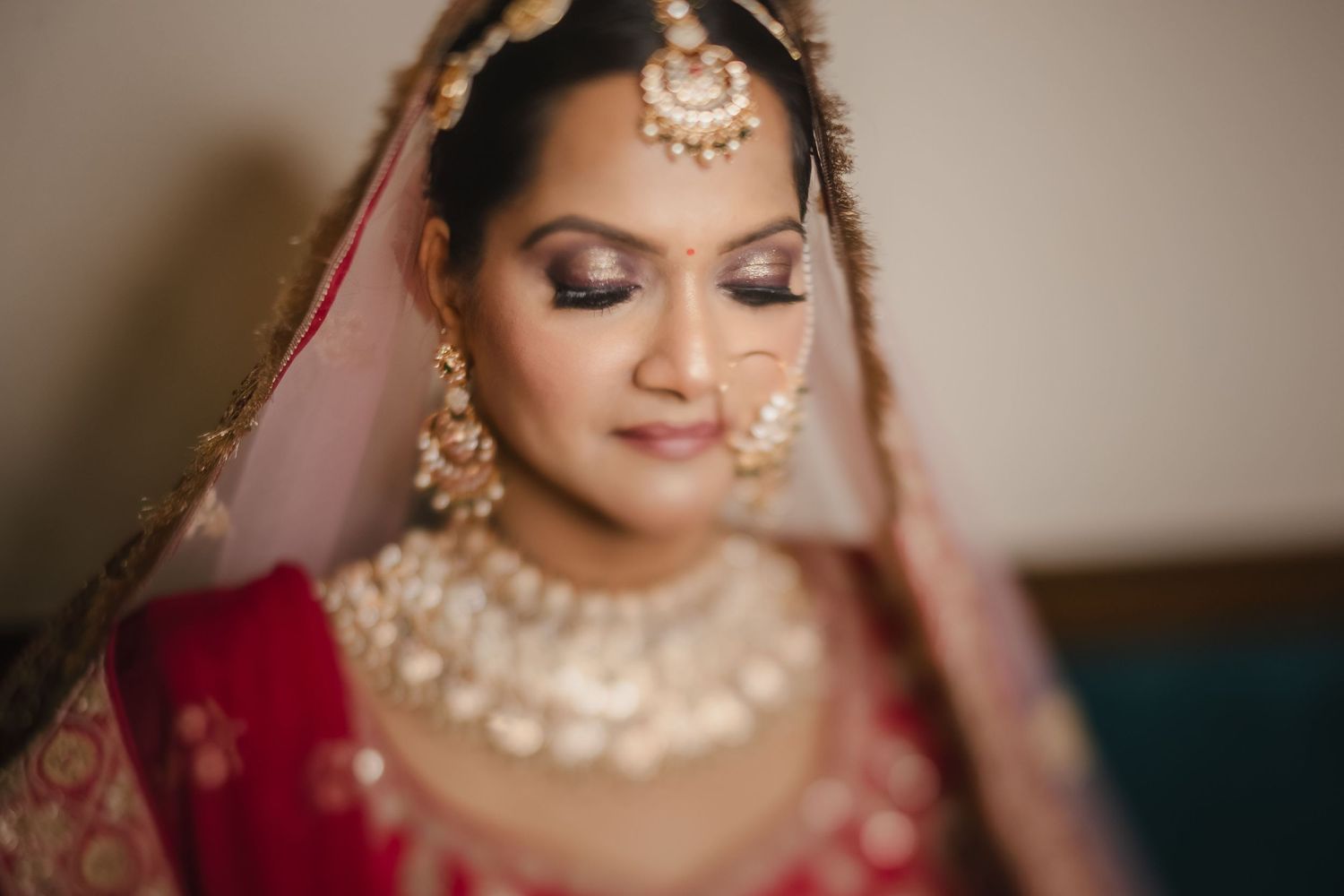 Traditional South Asian bride wearing elegant pearl jewelry and red embroidered attire with eyes closed in soft lighting.