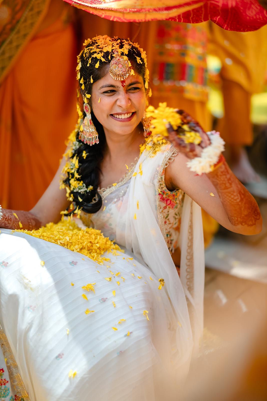 Traditional Indian haldi ceremony with person in white sari covered in yellow turmeric powder amid festive decorations.