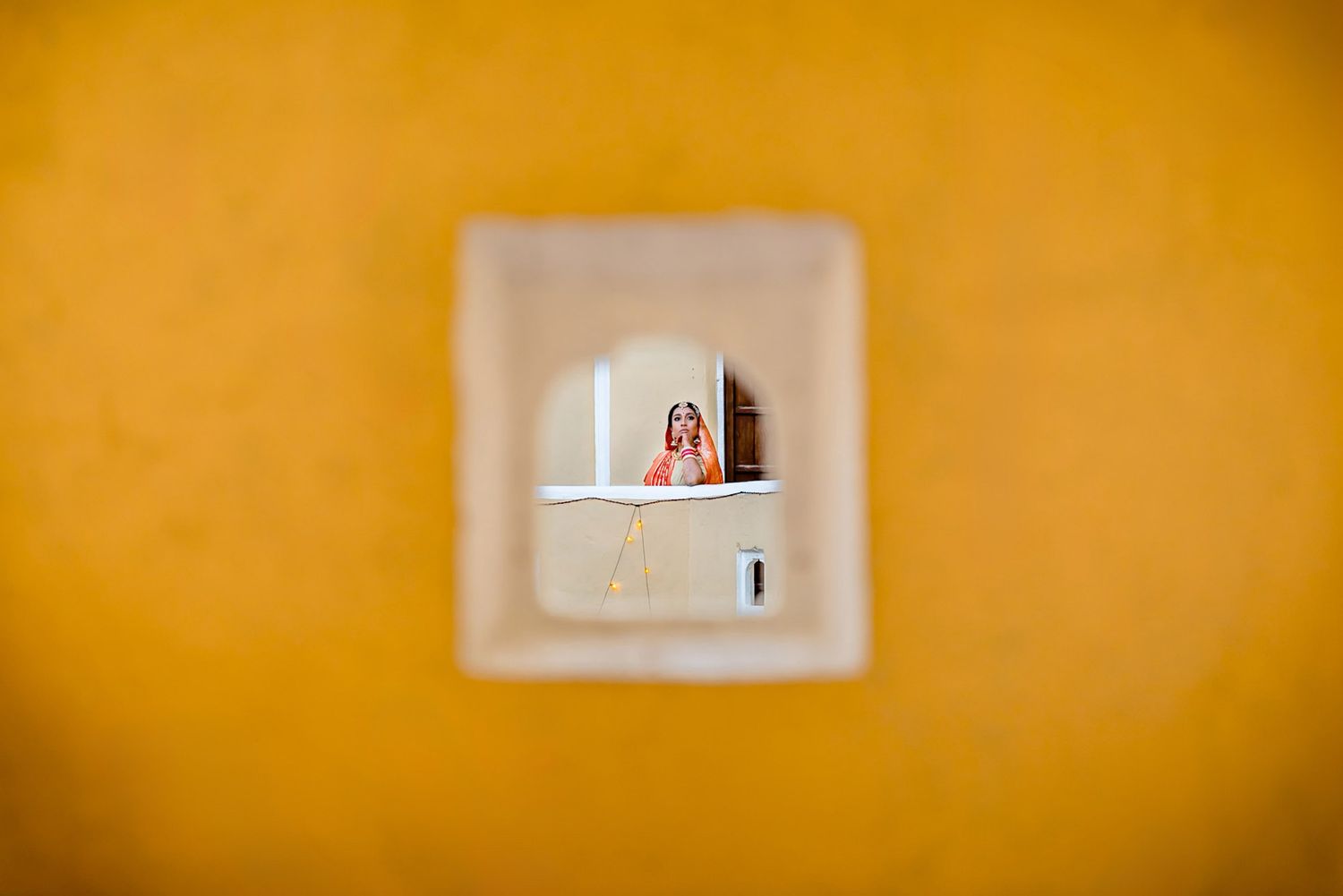A small window framed in white against a bright yellow wall shows a person through the opening.