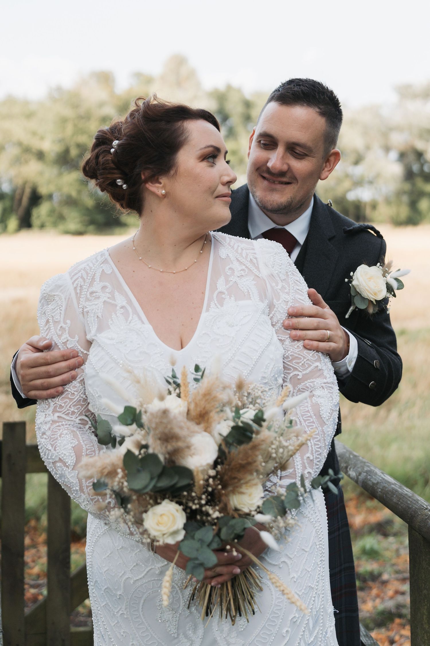 A bride holds a beautiful bouquet with pampas grass and roses while sharing an intimate moment during their outdoor wedding.