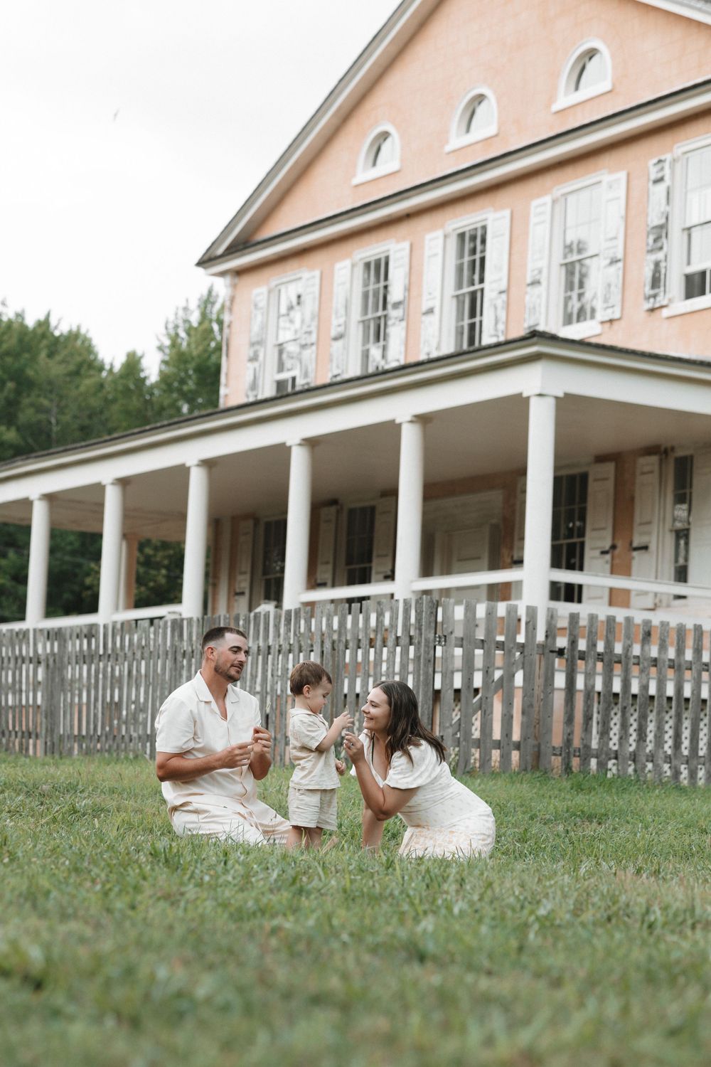 A family relaxes together on the lawn of a grand colonial-style house.