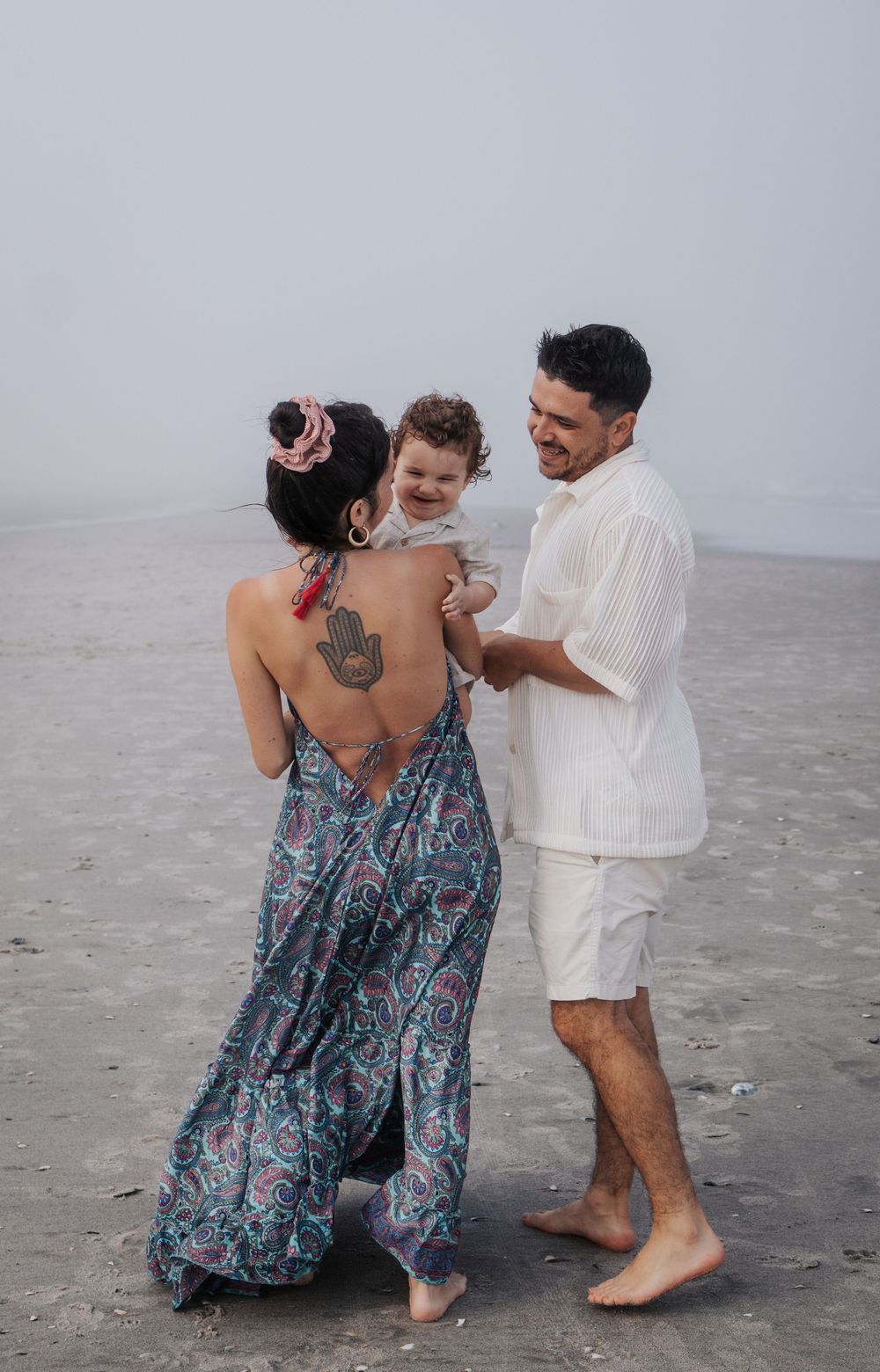 Family members share joyful interactions on an overcast beach.