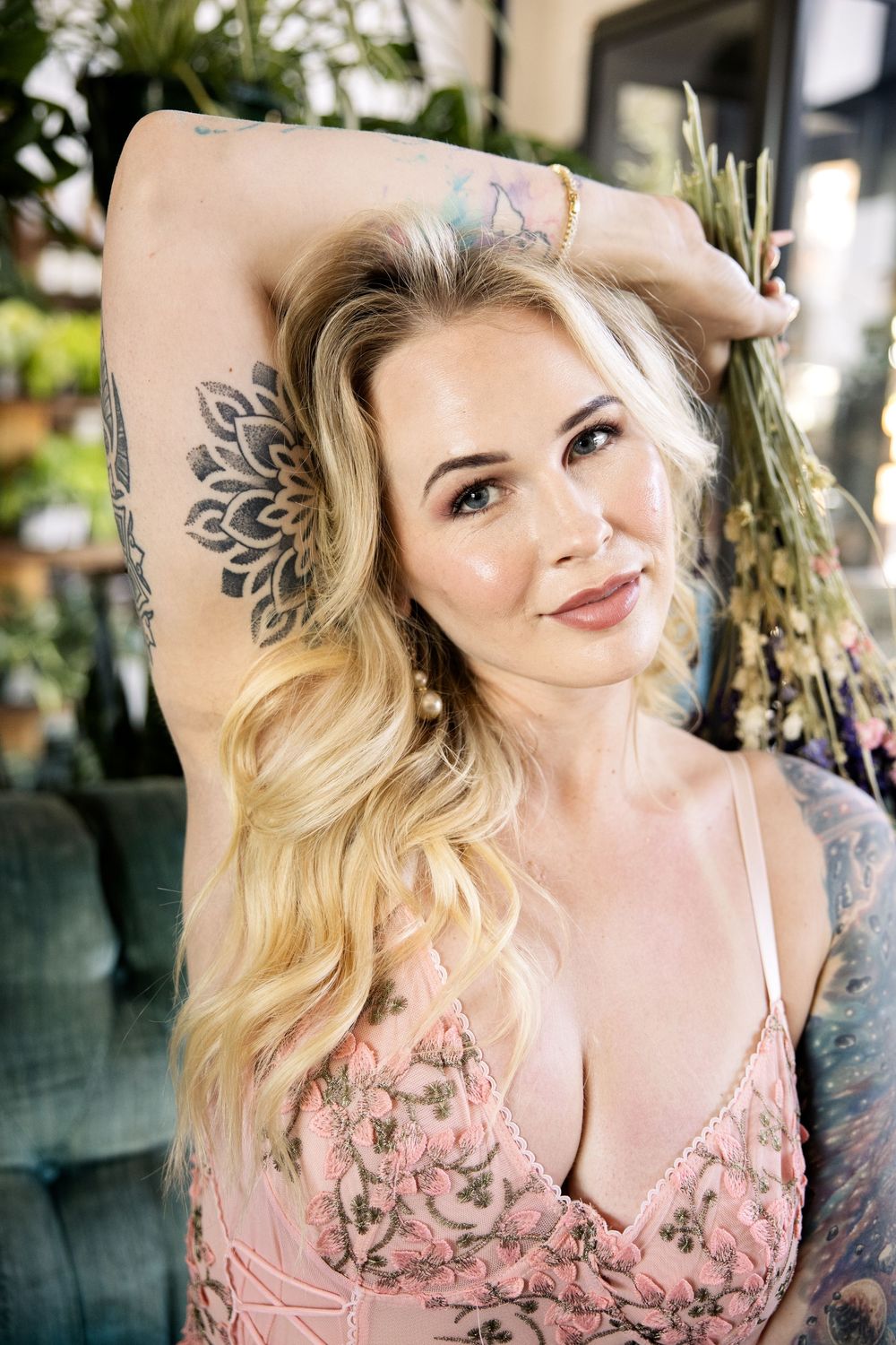 Artistic portrait in a conservatory featuring blonde hair, a pink top and decorative tattoo artwork.
