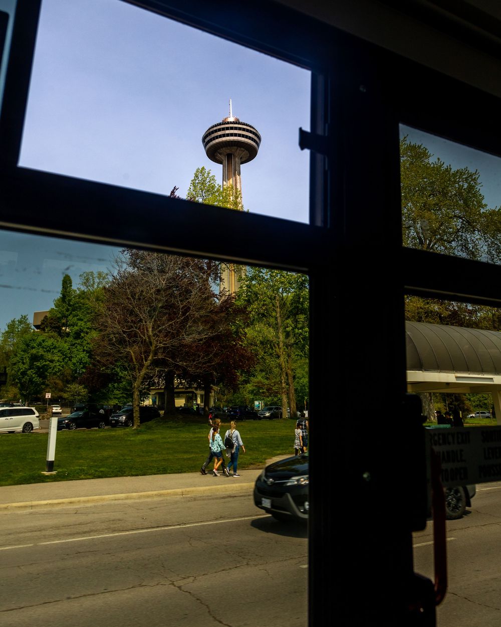 A panoramic view through windows showing a sun-lit parking area and trees.