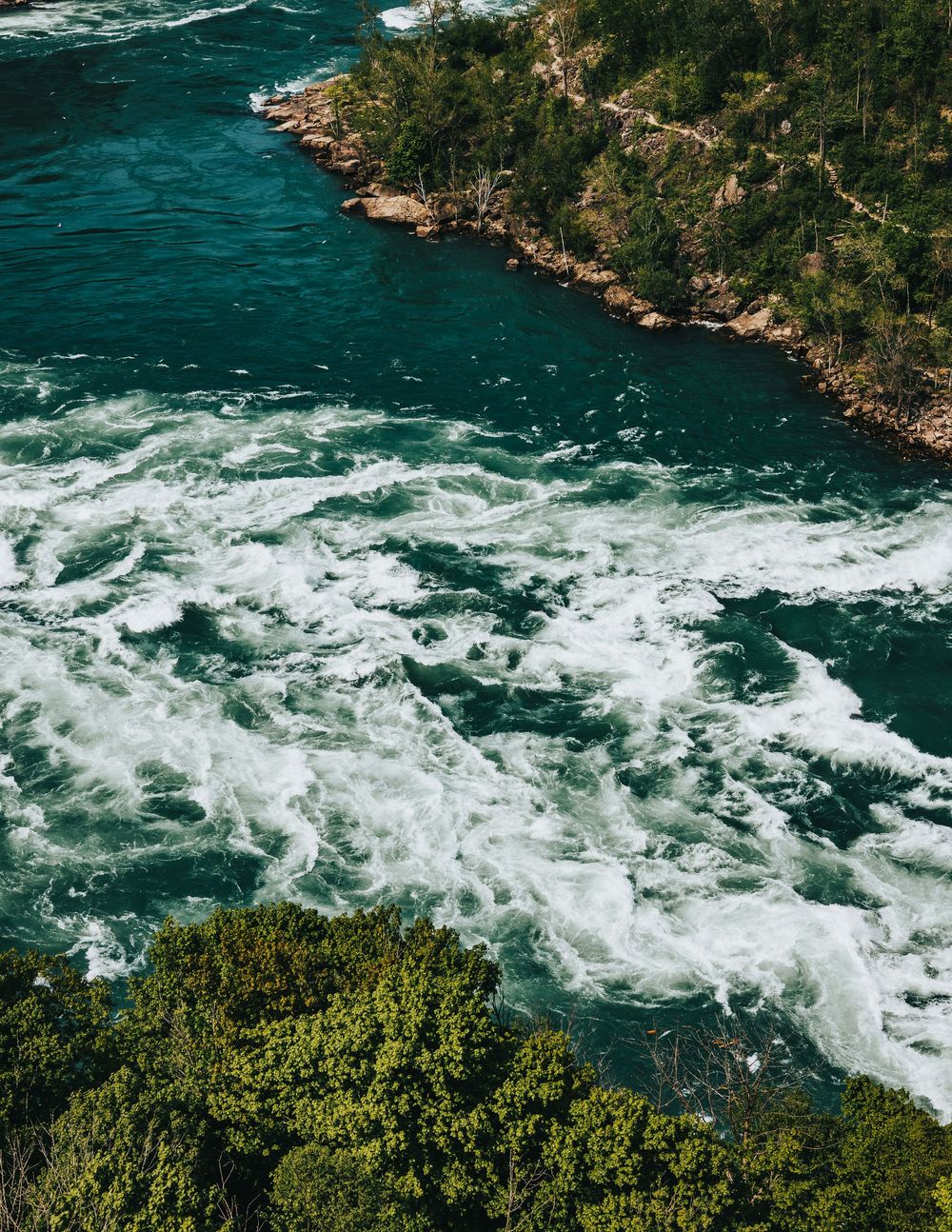 Aerial view of white water rapids flowing through a rocky gorge surrounded by green vegetation.