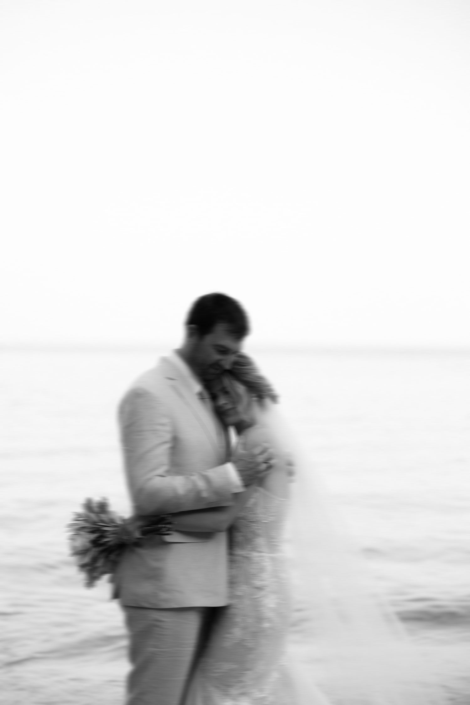 A blurred black and white romantic moment between newlyweds by the ocean.