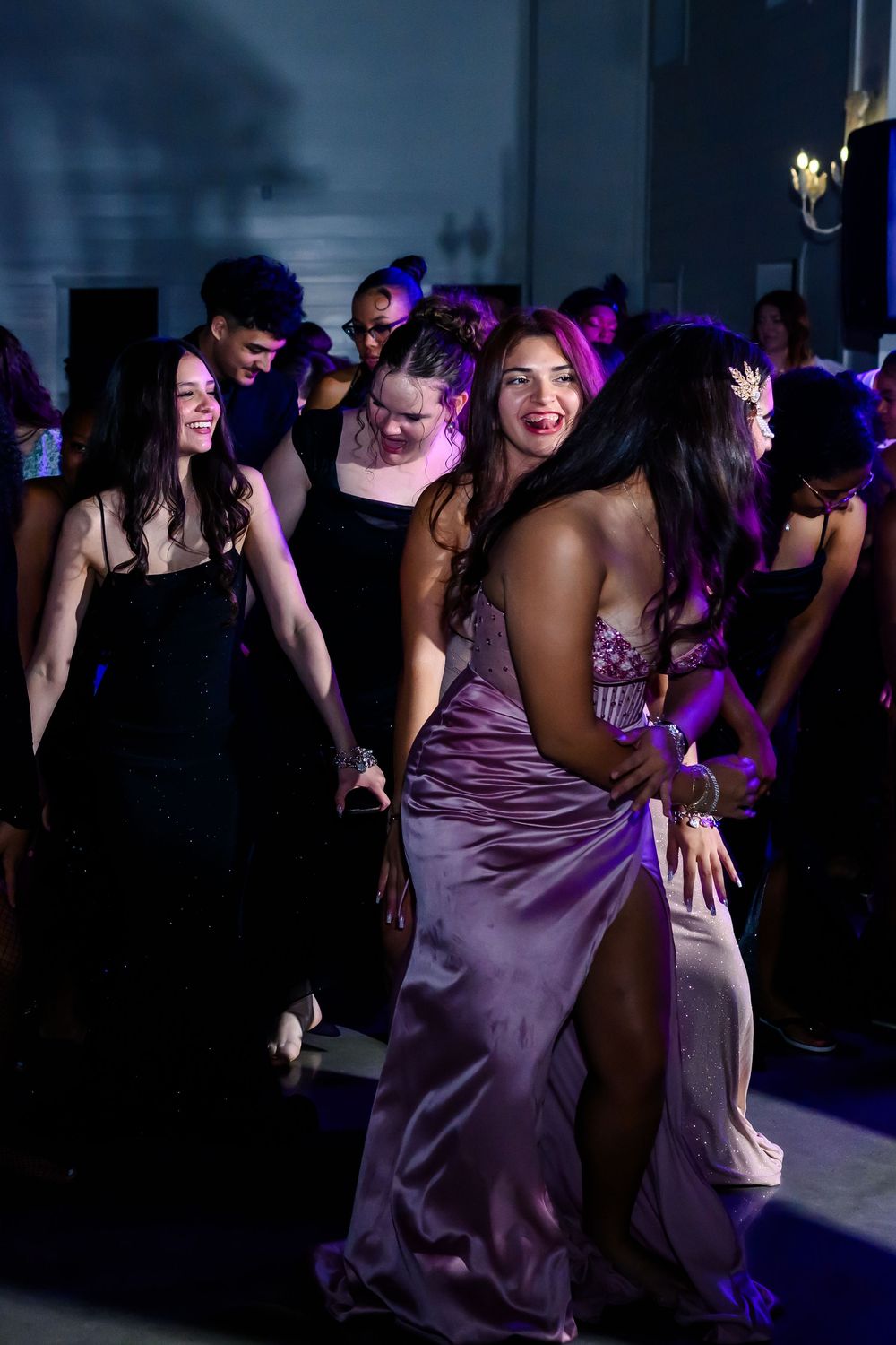 Wedding guests dancing and celebrating on a dimly lit dance floor with purple lighting effects.