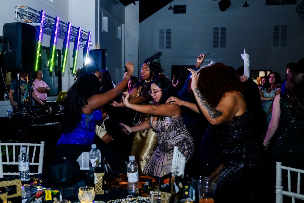 Enthusiastic dancers having fun at a lively party with colorful lighting and white chairs visible.