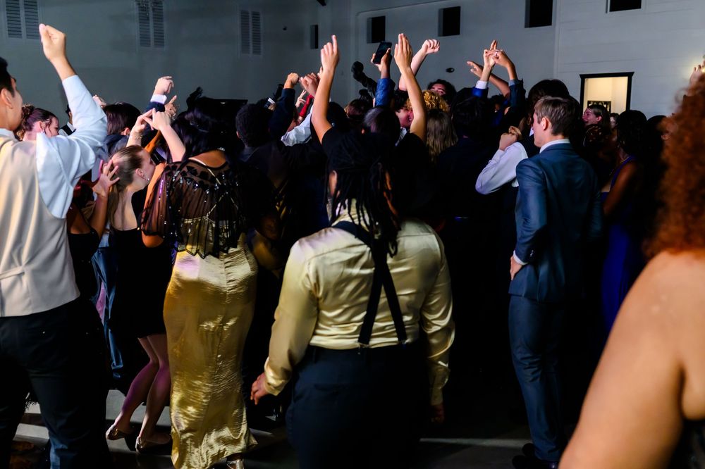 A crowd of party guests dancing and raising their hands on a dimly lit dance floor during a celebration.