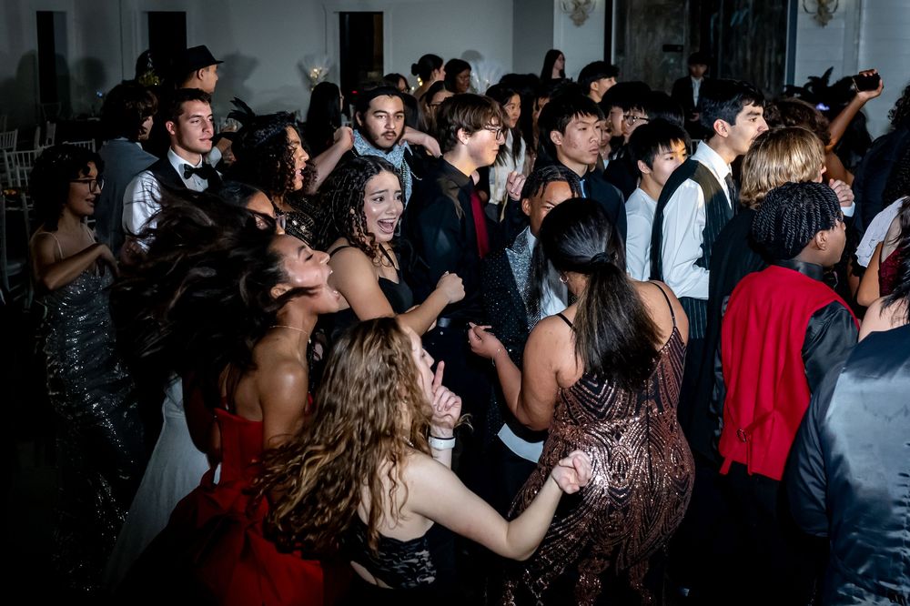 A dimly lit dance floor filled with formally dressed guests enjoying a celebration.