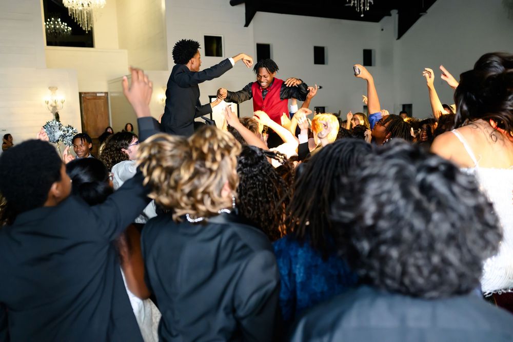 A lively crowd with raised hands dancing at an indoor event venue.