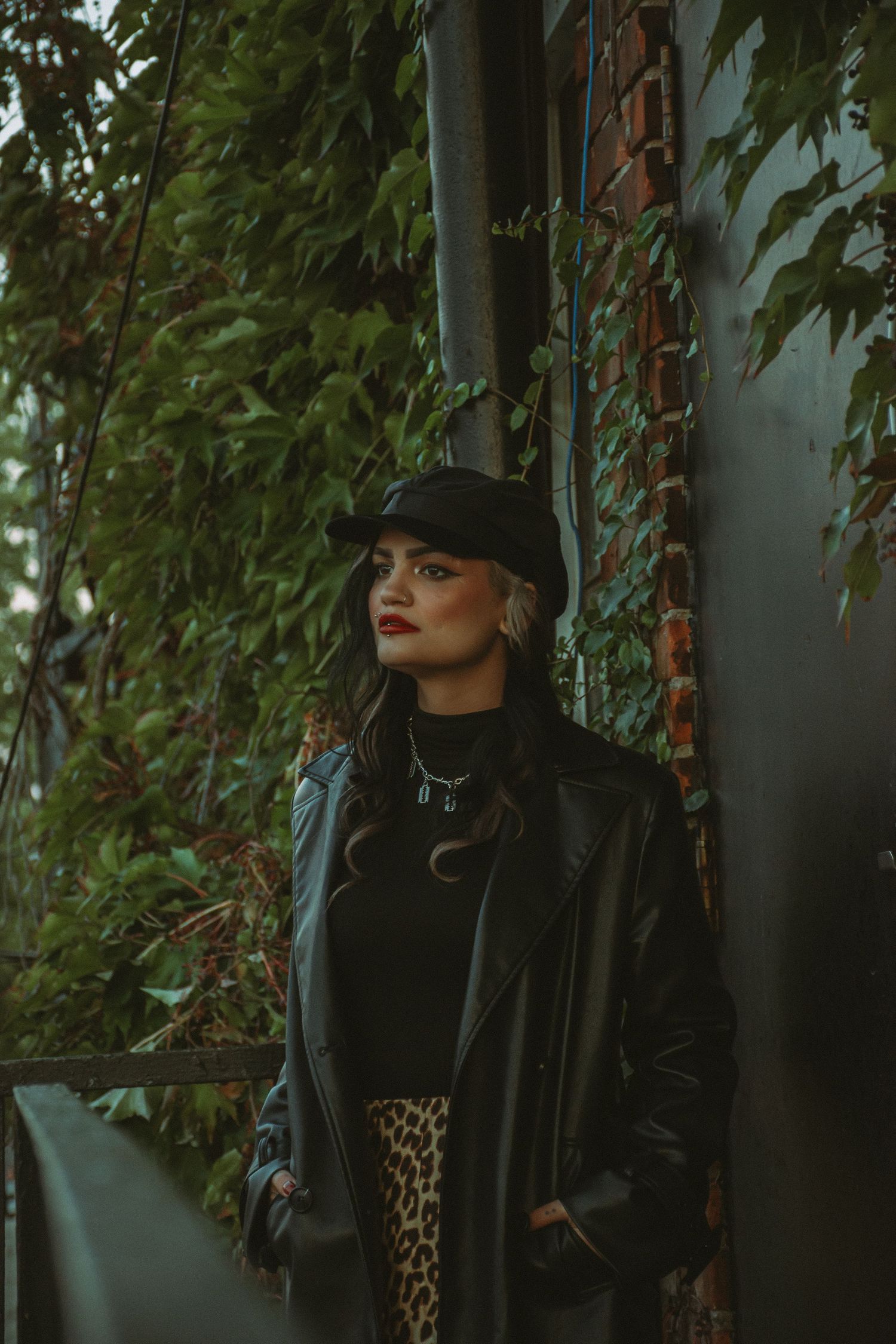 Urban fashion photography with black leather jacket and baseball cap against green foliage.