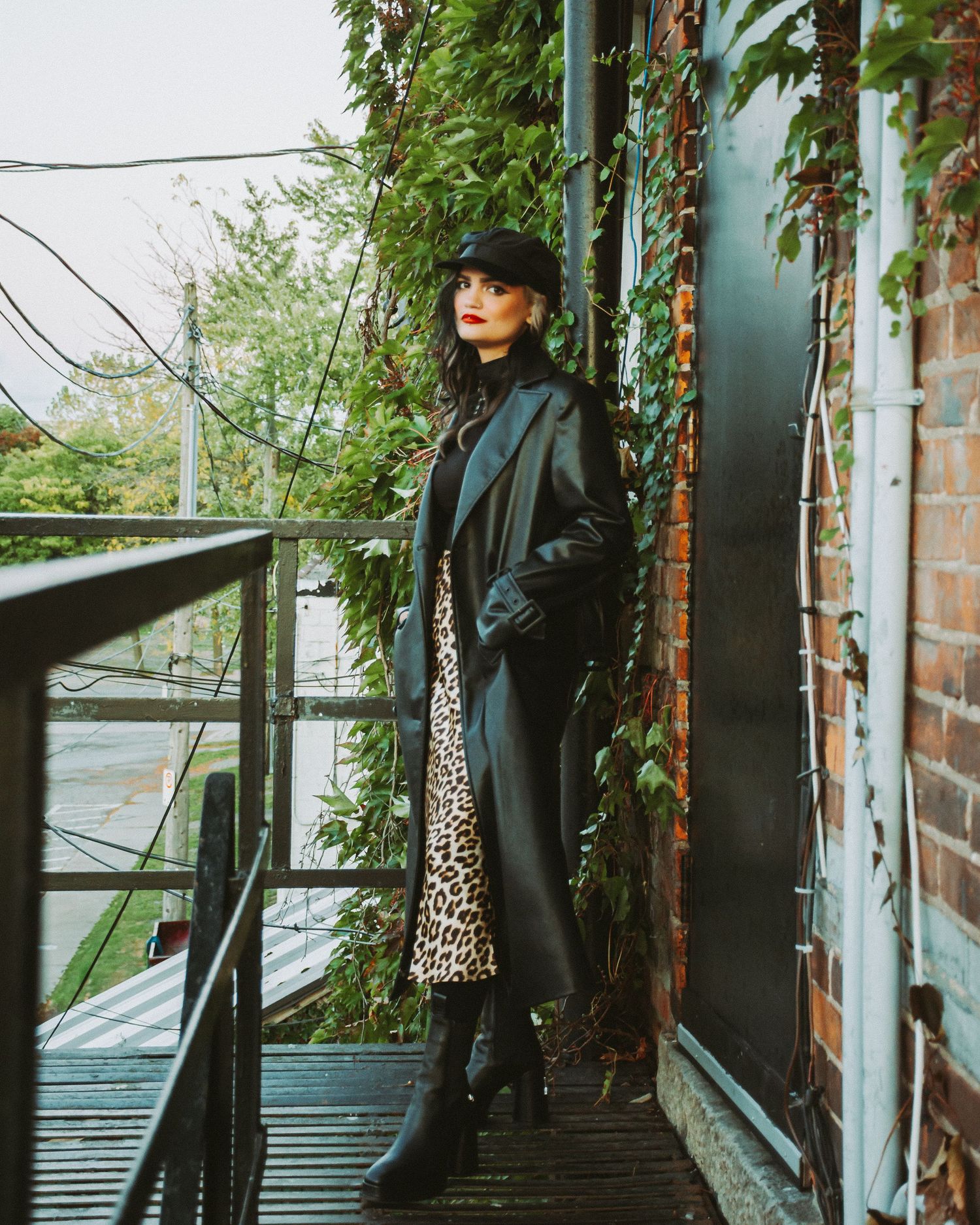 Fashion photography in an ivy-covered alleyway featuring dark clothing and urban aesthetics.