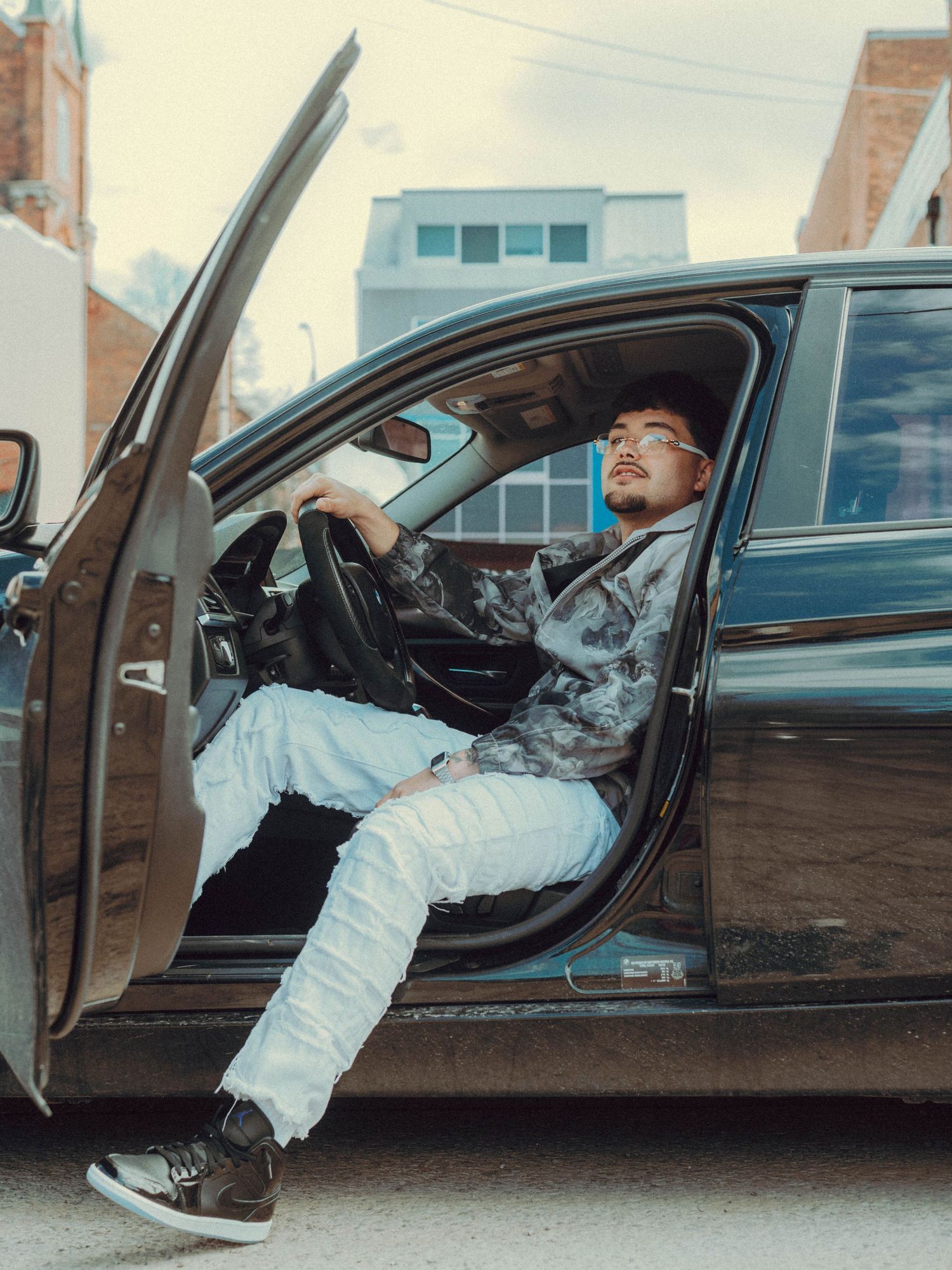 Multiple shots of someone lounging inside a luxury car with doors open against an urban backdrop.