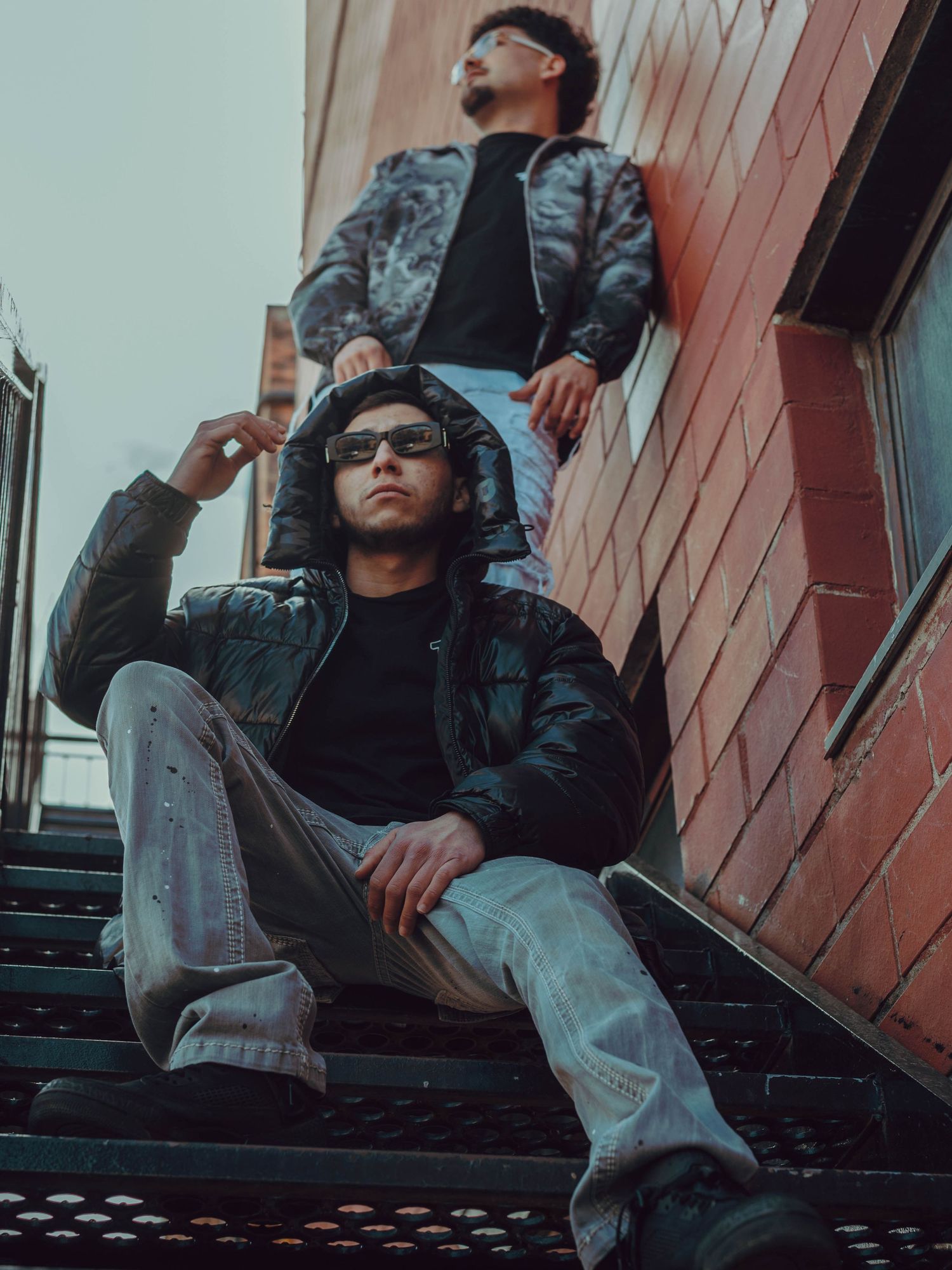 Someone wearing sunglasses and casual clothing poses on outdoor steps in an urban setting.