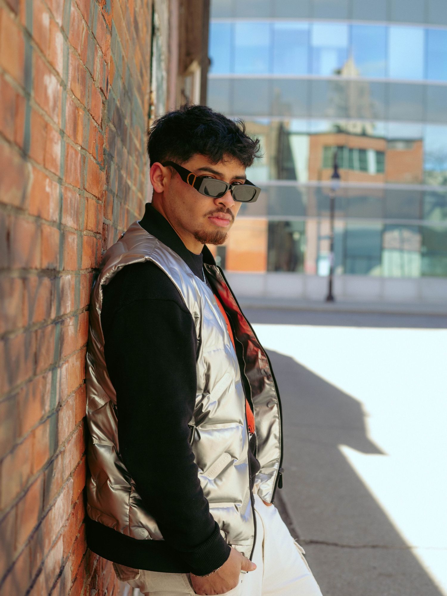 A fashion photoshoot featuring someone in a black vest and light pants against modern architecture.