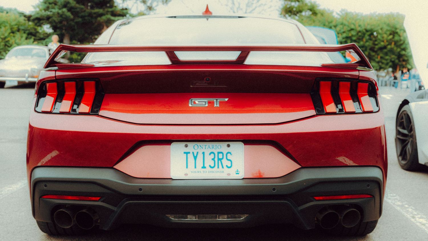 Red sports car rear view showing sleek taillights and exhaust system on a sunny day.