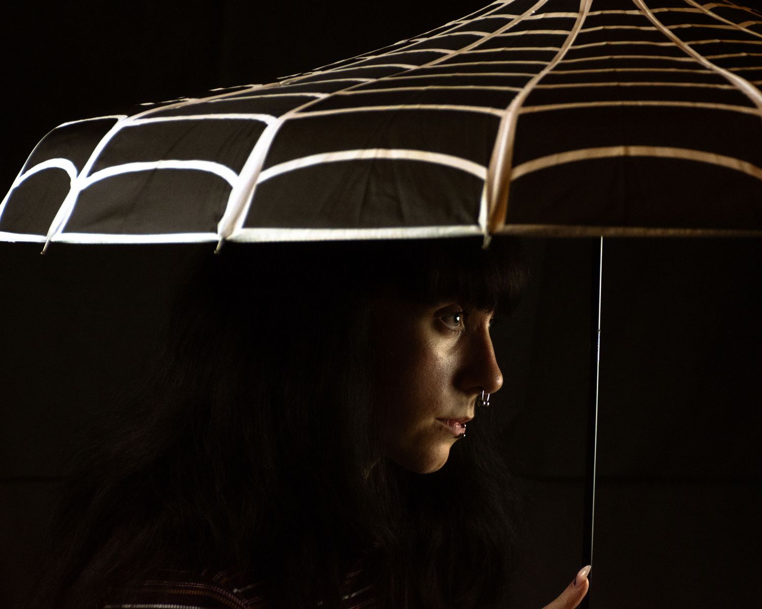 A dramatic silhouette under a parasol or umbrella in dark lighting.