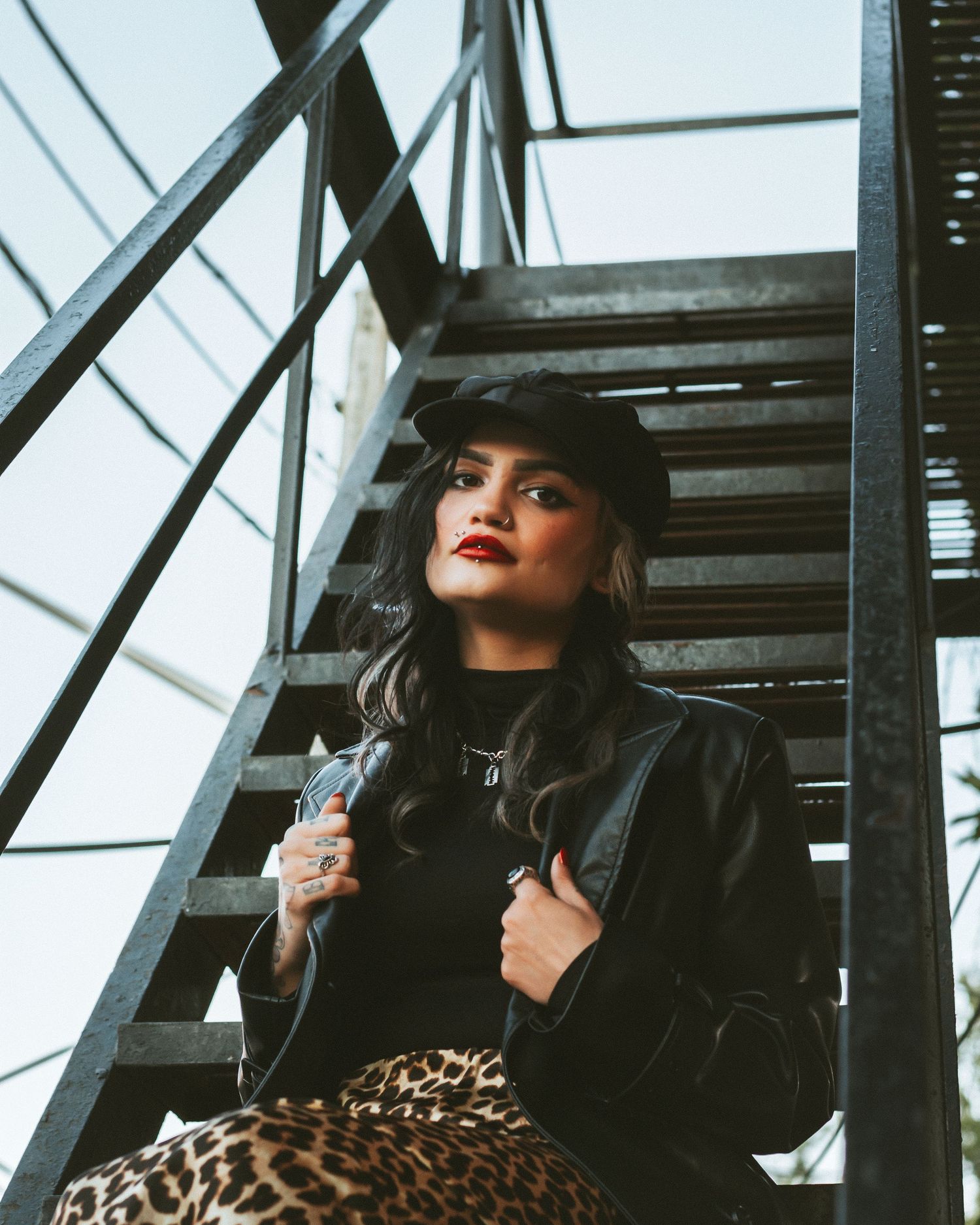 Stylish outfit featuring black leather jacket and leopard print against industrial staircase backdrop.