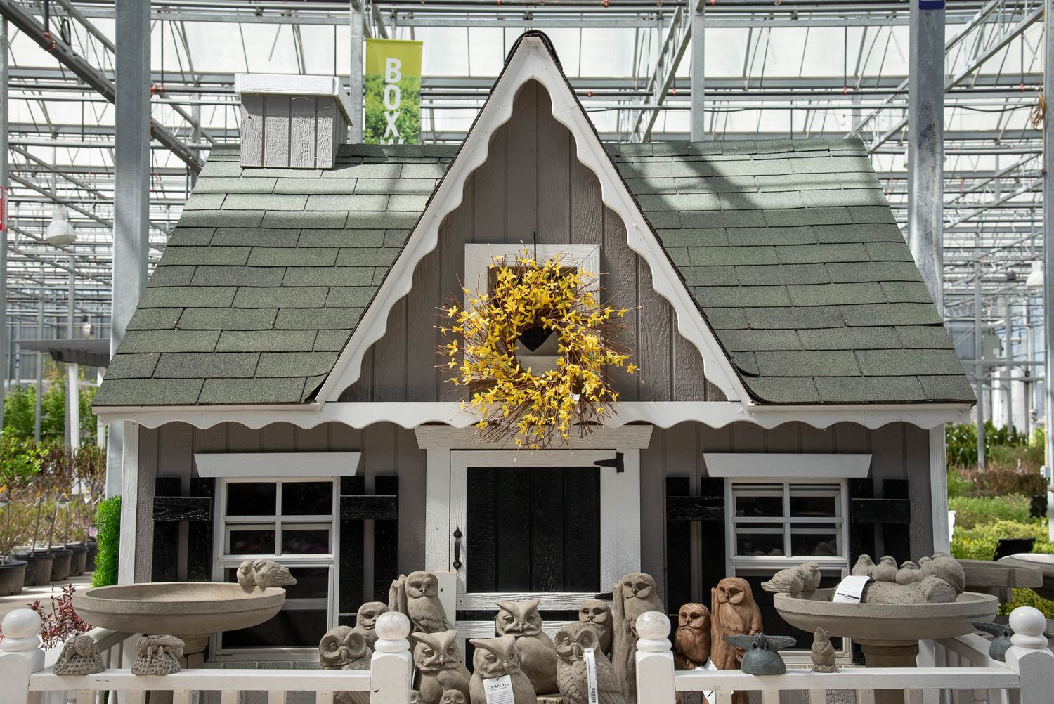 Small gray and white playhouse with a yellow sunflower wreath displayed inside Bradford Greenhouse in Barrie, ON