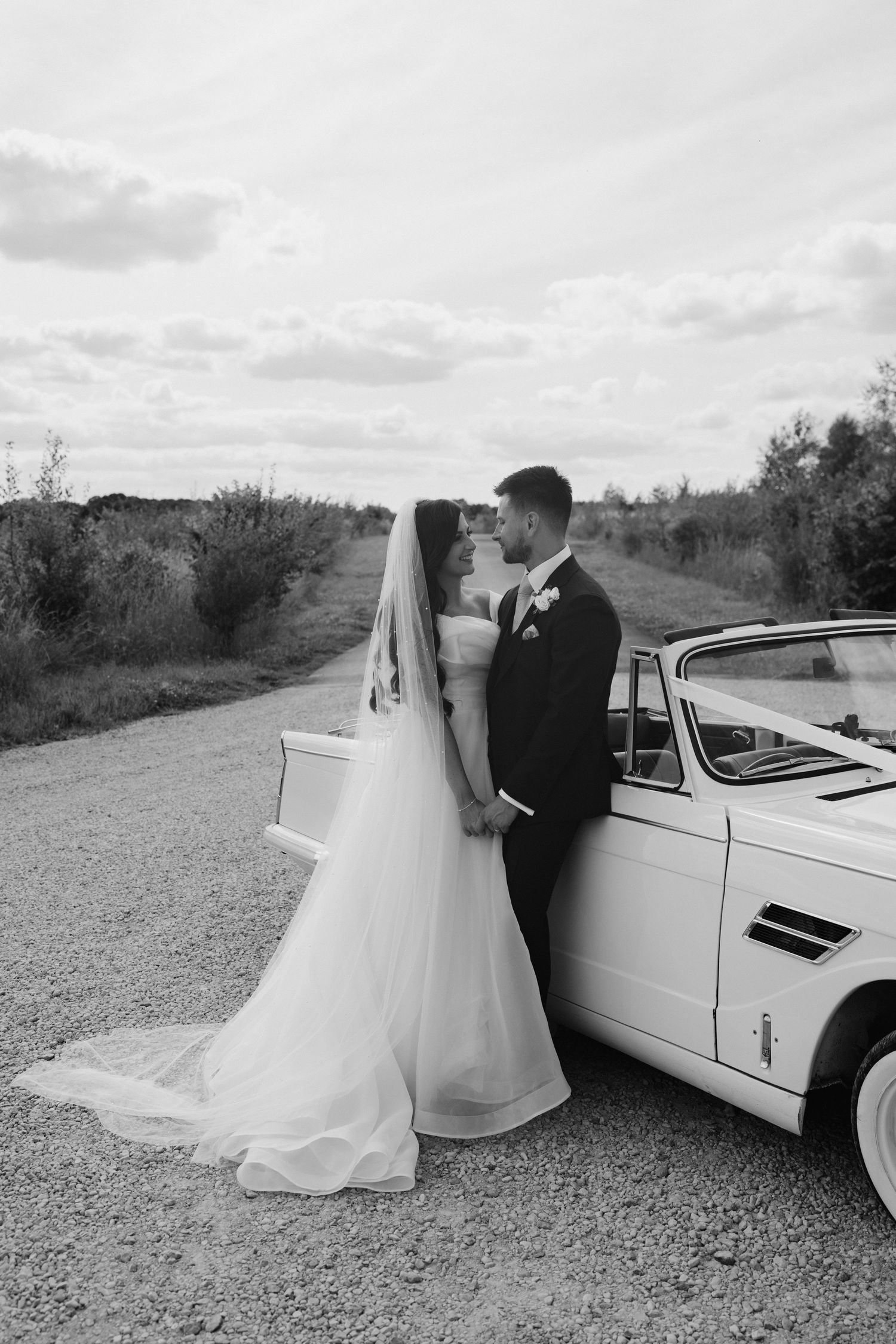 bride and groom leaning against vintage car at yardspace old gore in cirencester