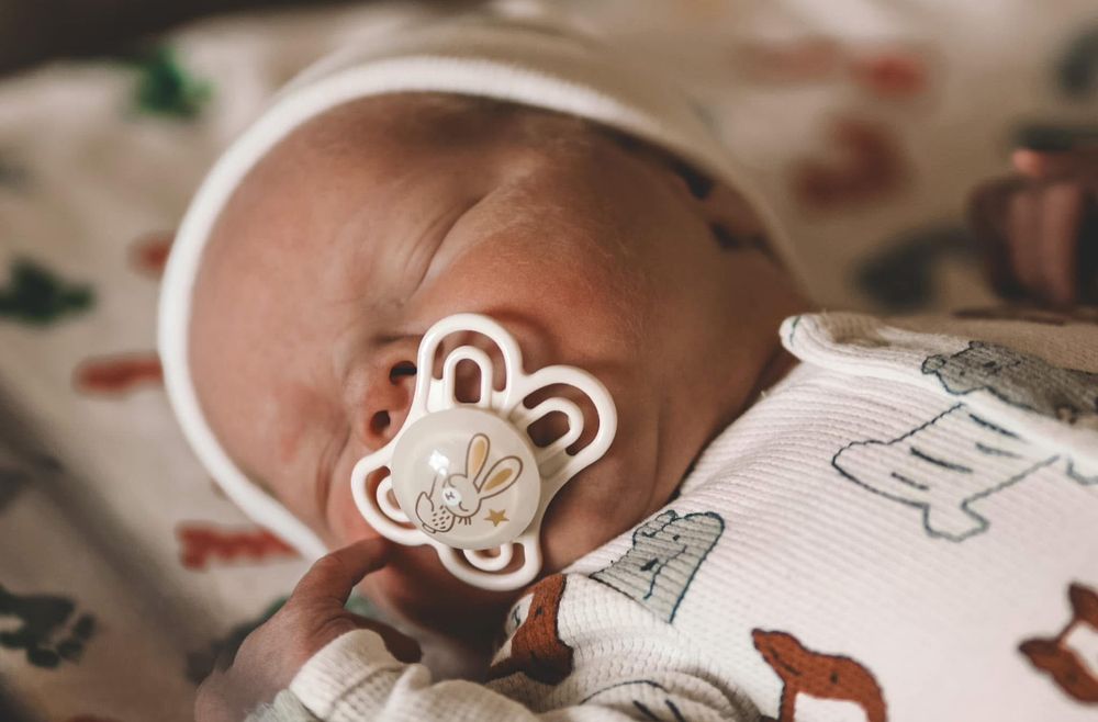 Close-up of a sleeping newborn baby with a bunny pacifier wearing an animal print onesie.
