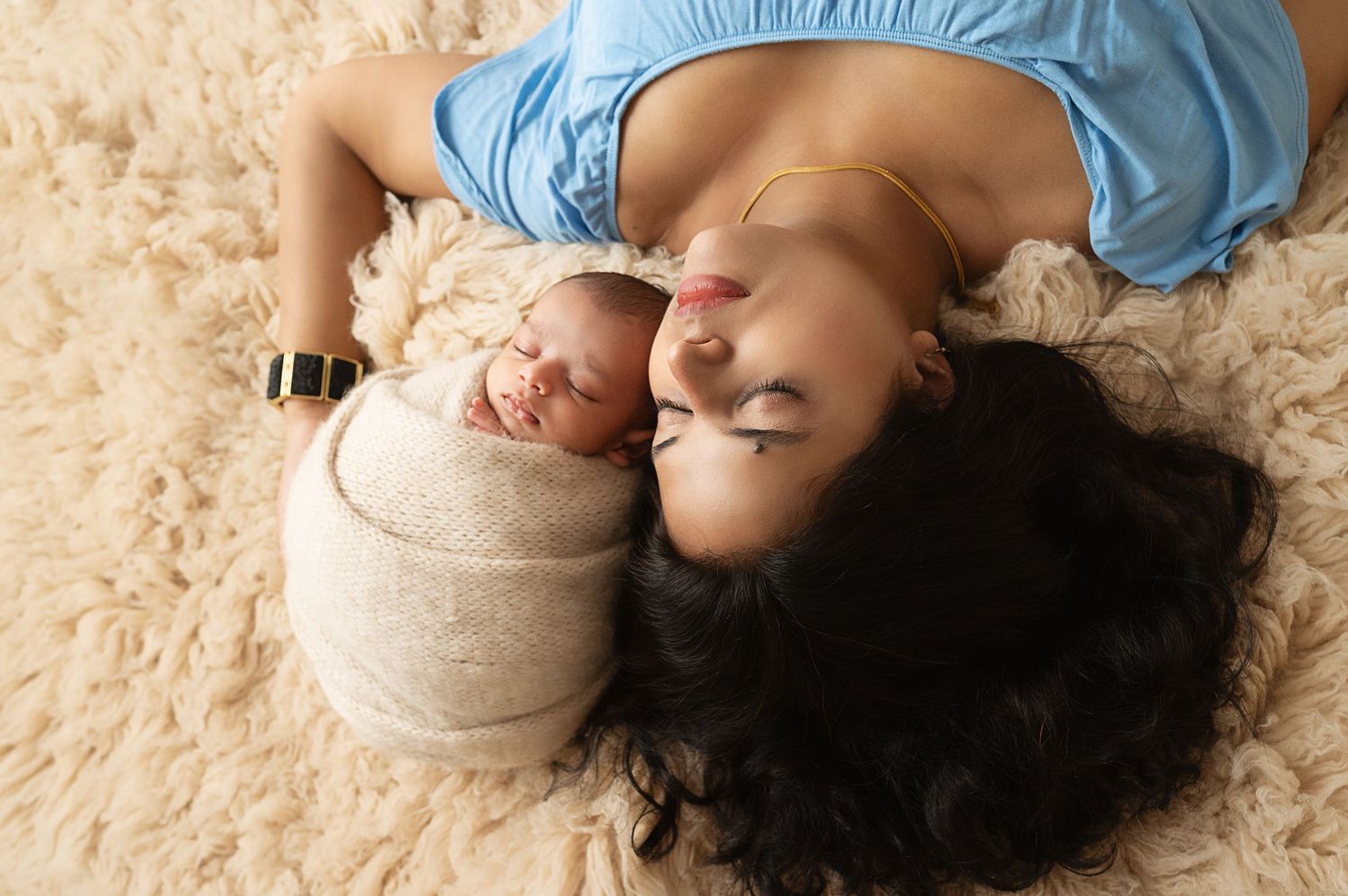 Mother and newborn baby lying together on beige carpet during intimate lifestyle photoshoot.