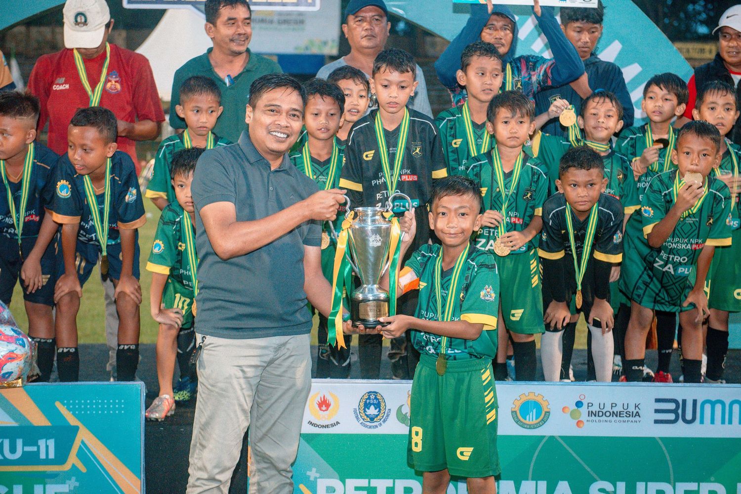 Youth soccer team in green uniforms celebrates with trophies and medals after winning a championship tournament.