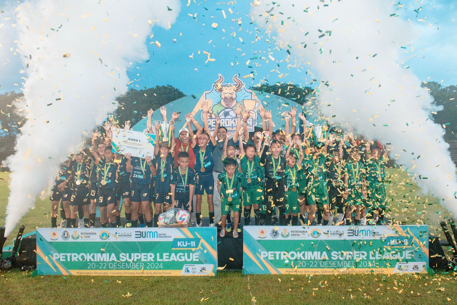 Soccer team celebrates championship victory with confetti and trophy on field under blue sky.