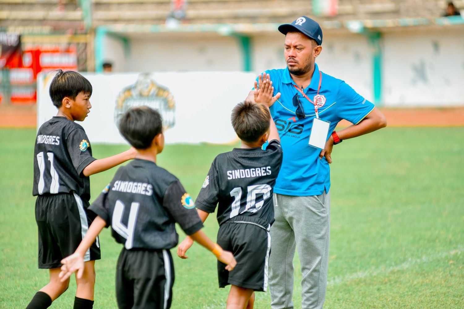 Youth soccer players in black jerseys practice drills with a coach in blue on a grass field.