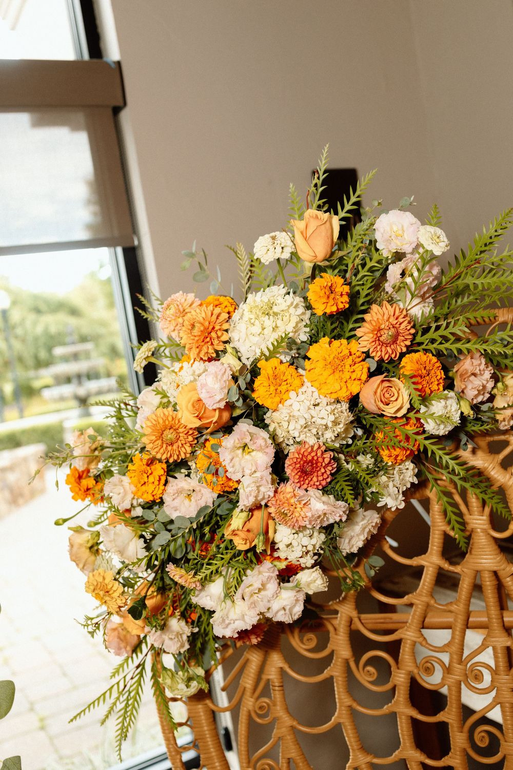 Orange and white floral arrangement with greenery decorating a woven rattan chair.