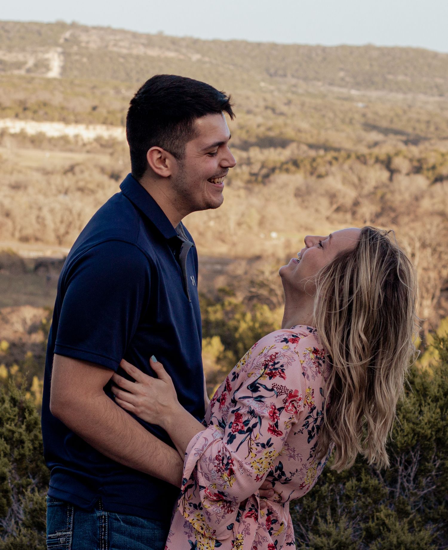Couple shares a tender moment in a sunlit field with tall grass and trees in the background.