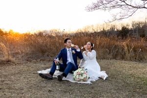 A couple laughs together while sitting on a blanket outdoors during their wedding photo session at golden hour.