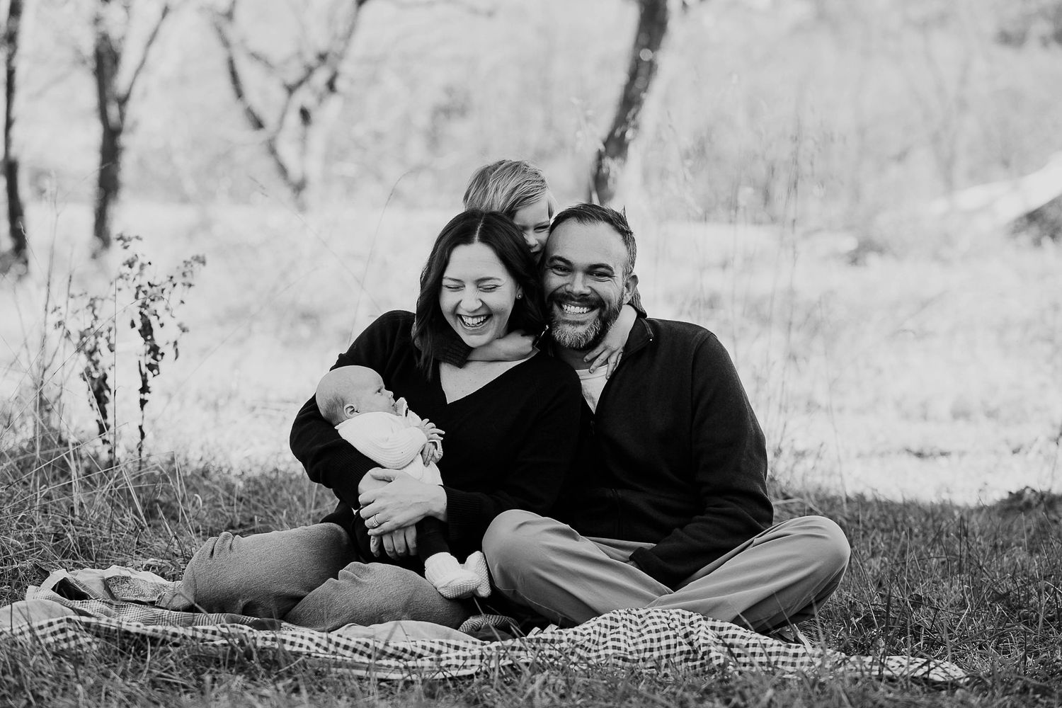 Black and white portrait of a family relaxing together on a blanket outdoors.