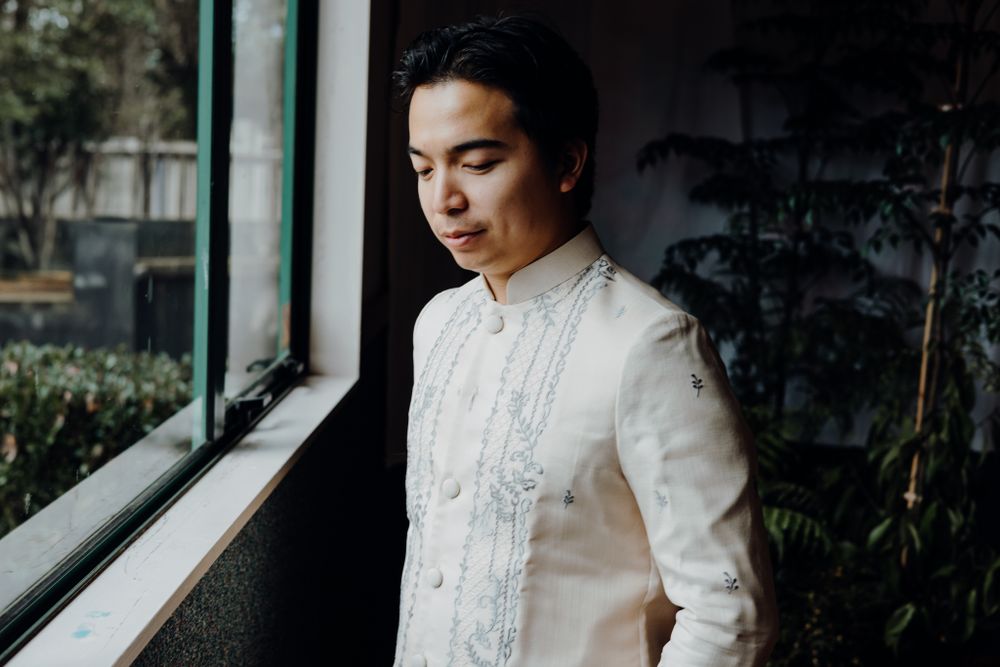 Elegant white Barong Tagalog with intricate embroidery detail near window.