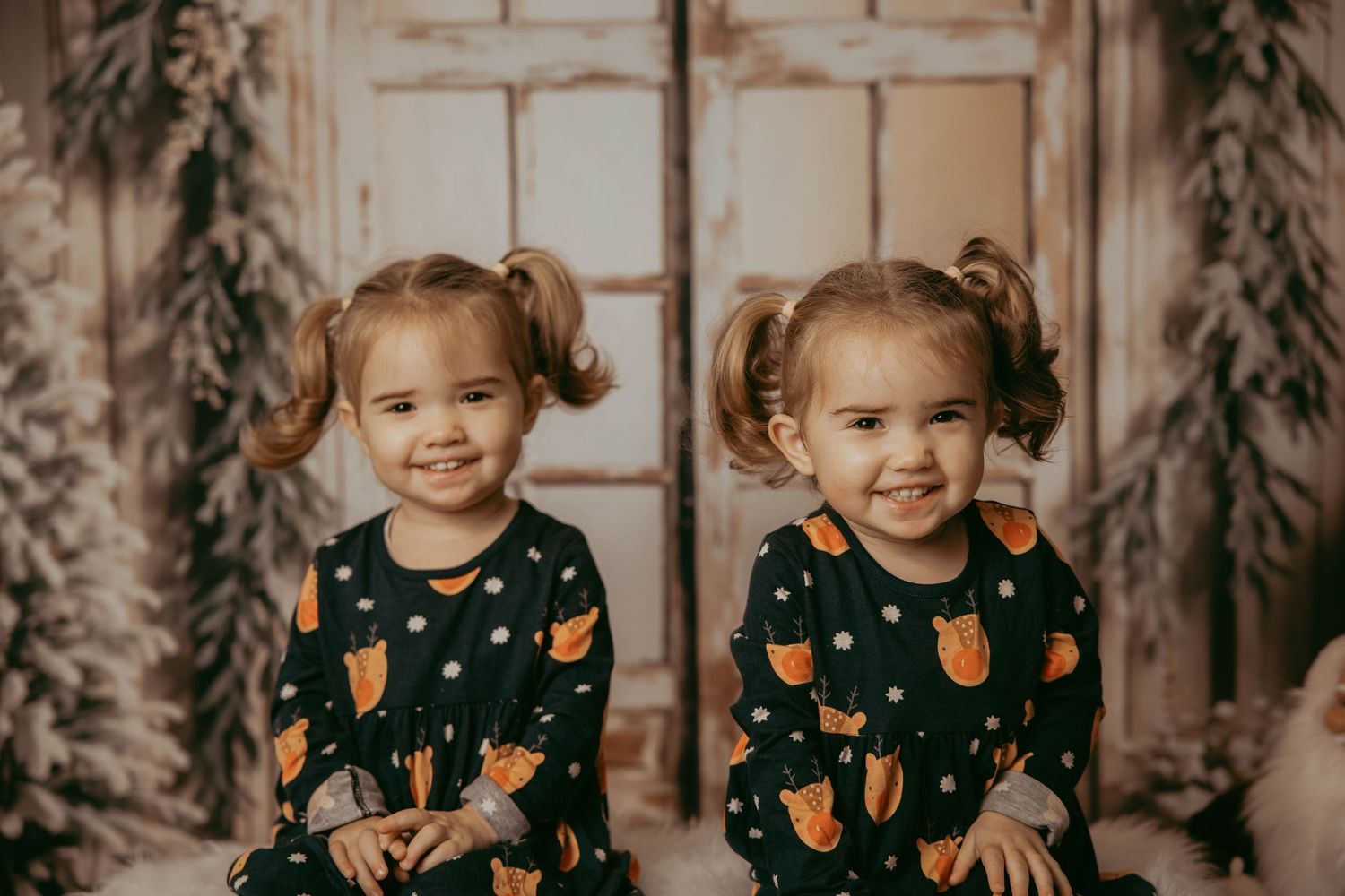 Matching sisters pose in holiday outfits with festive decorations and window backdrop.