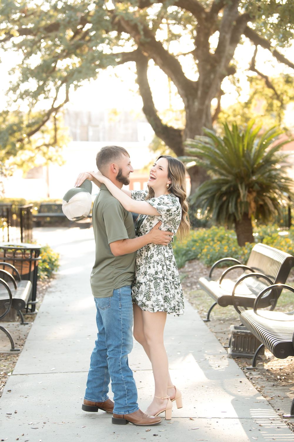 Romantic engagement session on park pathway with benches and palm trees at sunset.