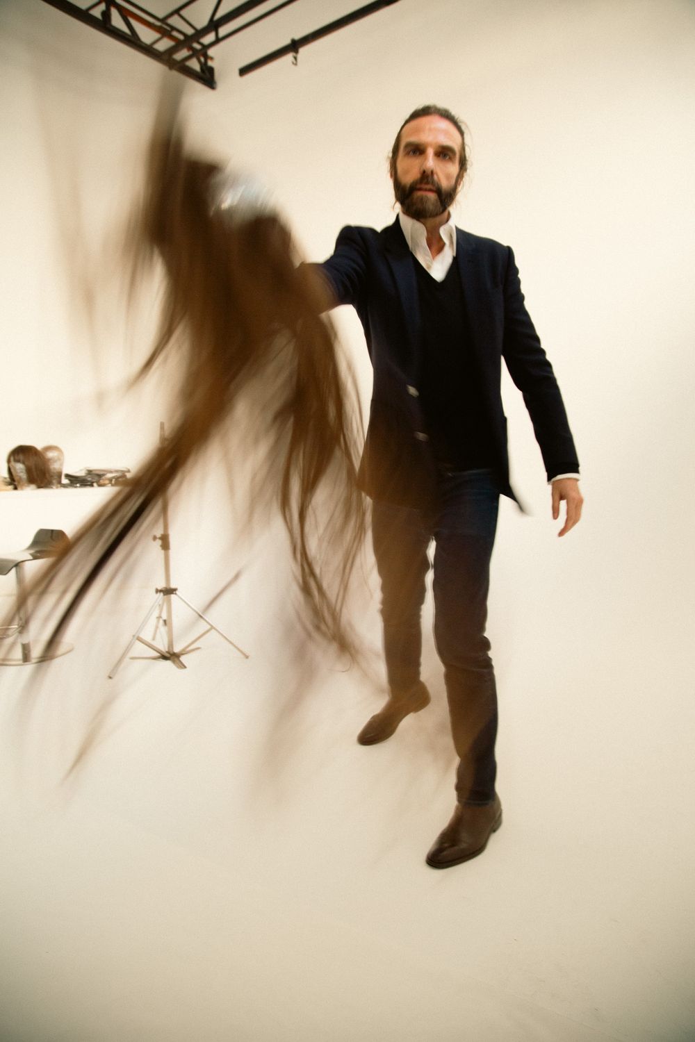 Dynamic fashion photo with motion blur effect showing someone in a dark suit against a white studio backdrop.