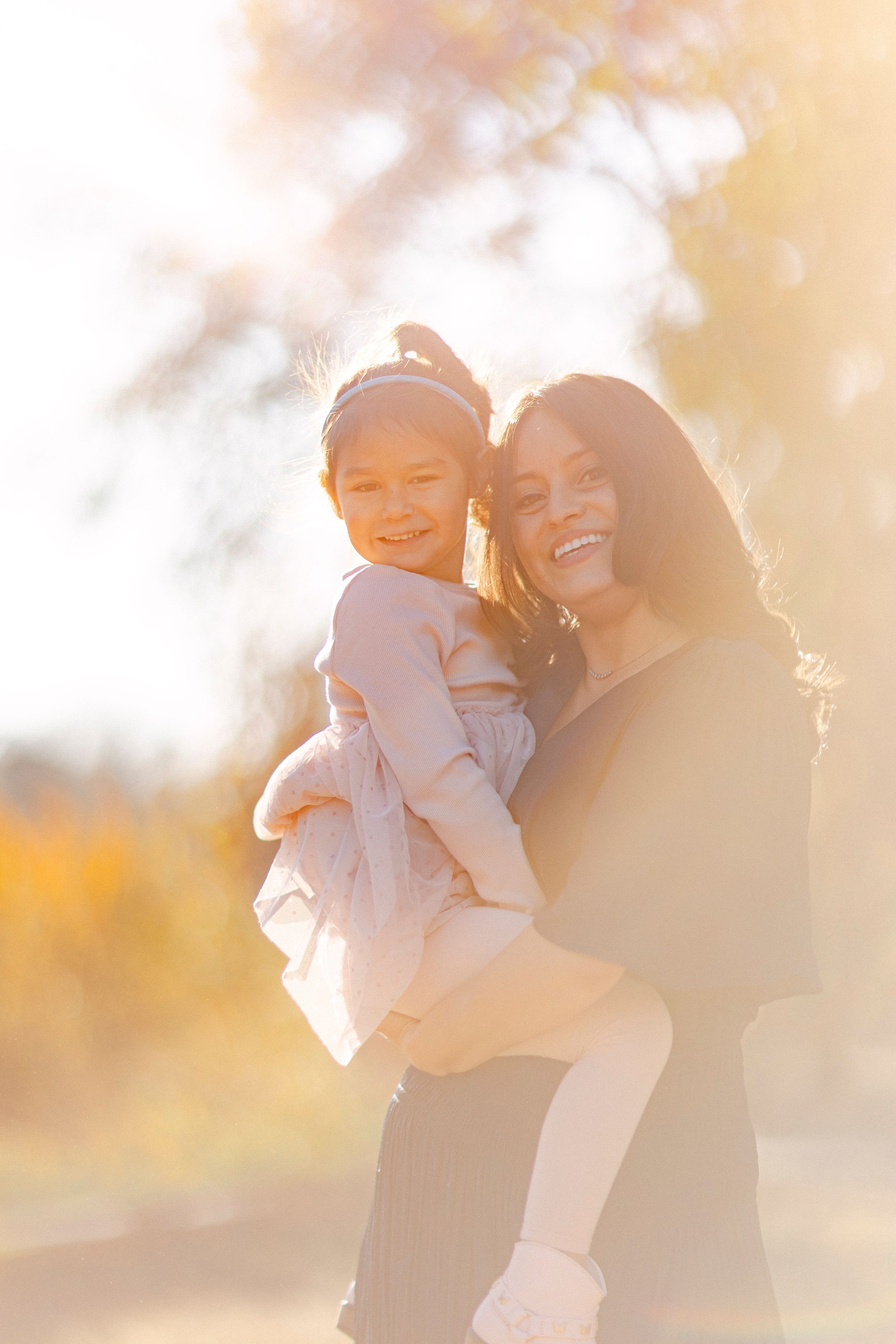 Parent and child share joyful laughter during sunny outdoor photoshoot.