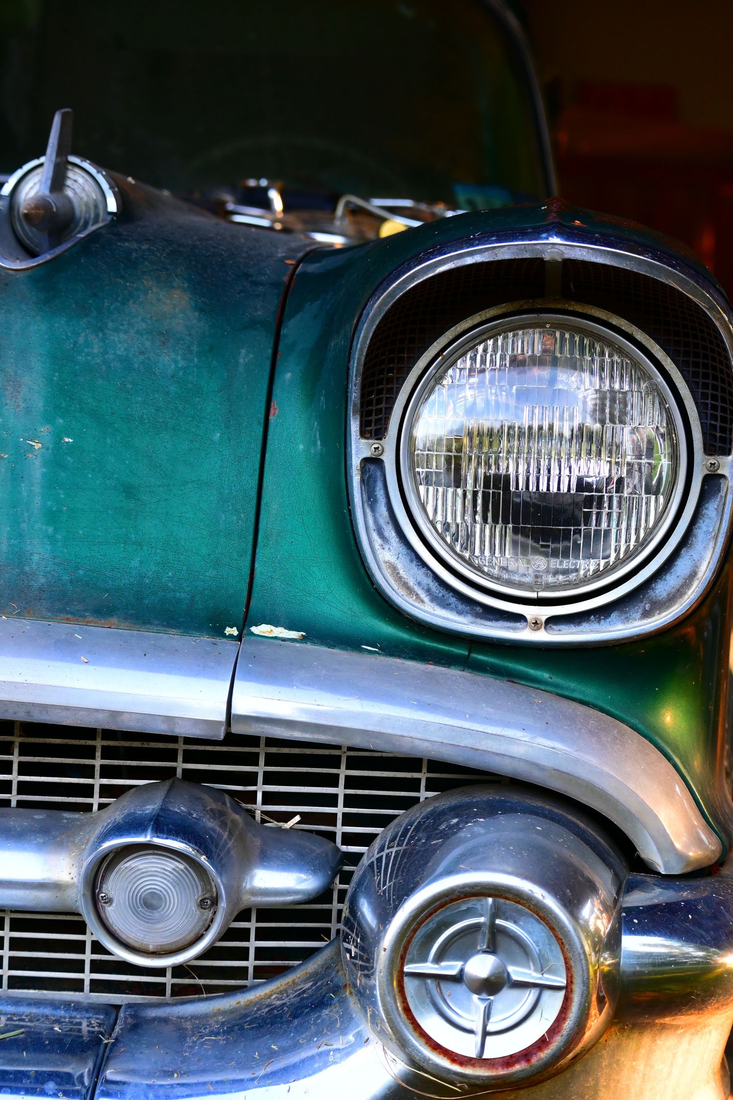 The left light assembly and grill of an aqua blue 1957 Chevy.